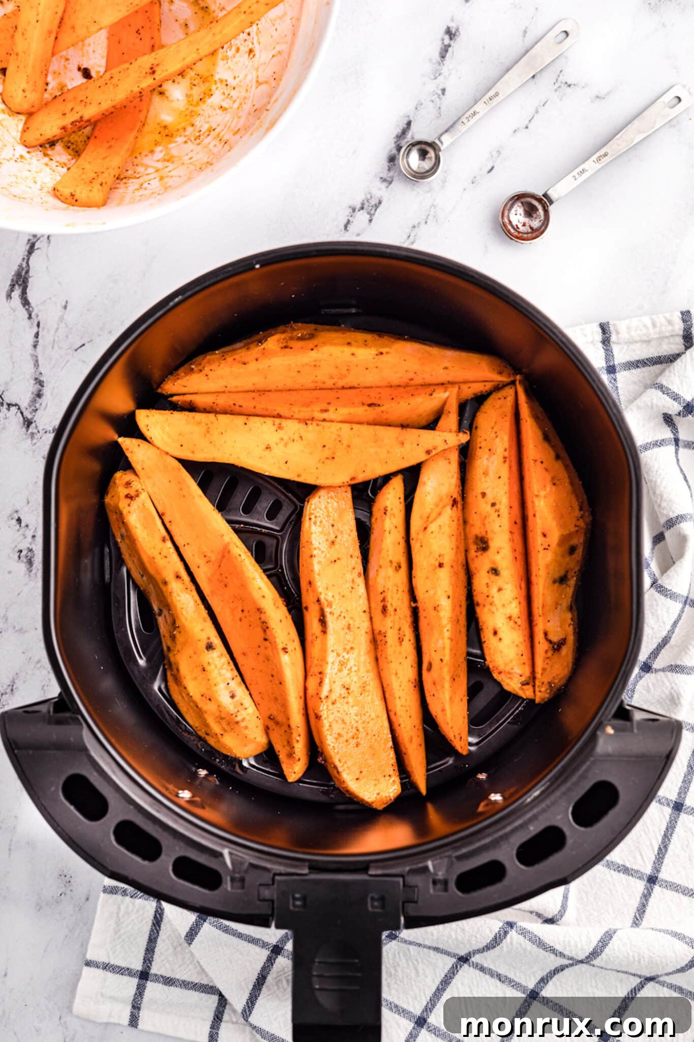 Sweet potato wedges being placed into an air fryer basket.