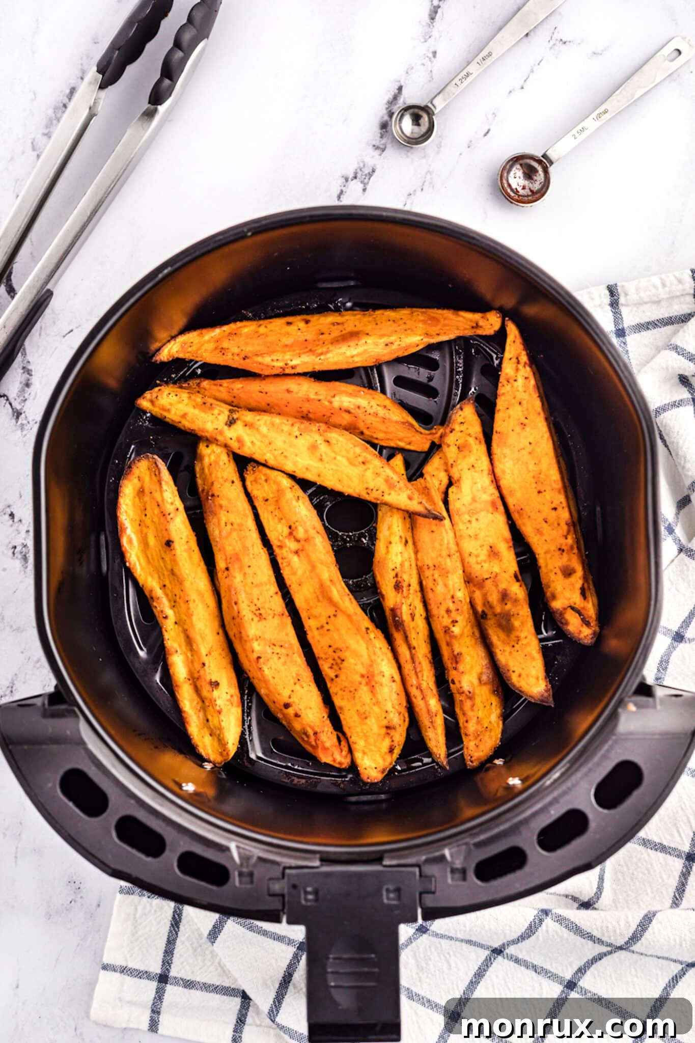 Partially cooked sweet potato wedges inside an air fryer, beginning to brown.