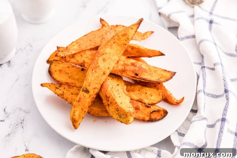 Air fryer sweet potato wedges piled up on a white plate, garnished with fresh herbs.