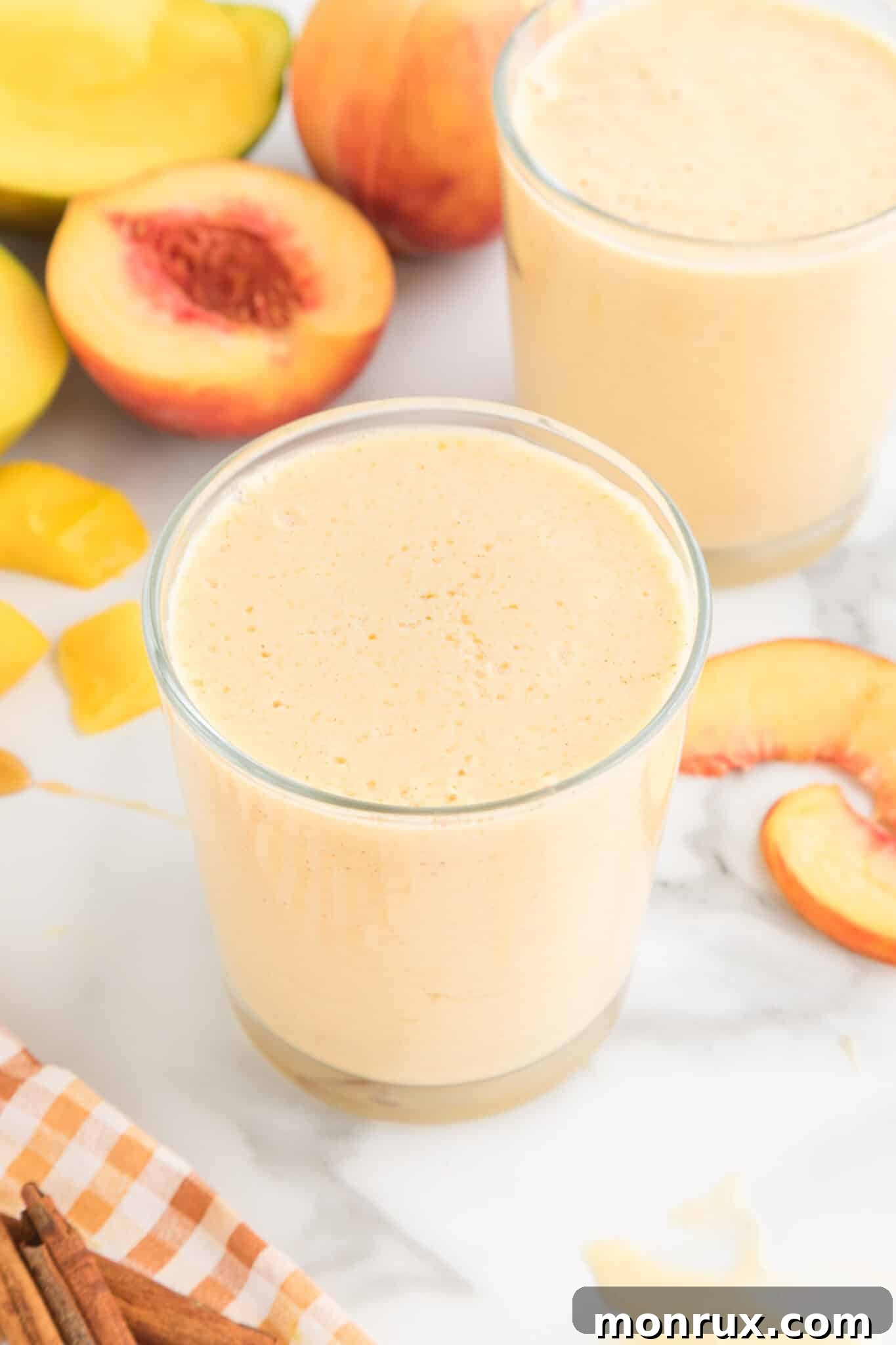 A vibrant glass of Mango Peach Smoothie, garnished with fresh fruit, sits on a rustic wooden table, evoking a sense of summer refreshment.