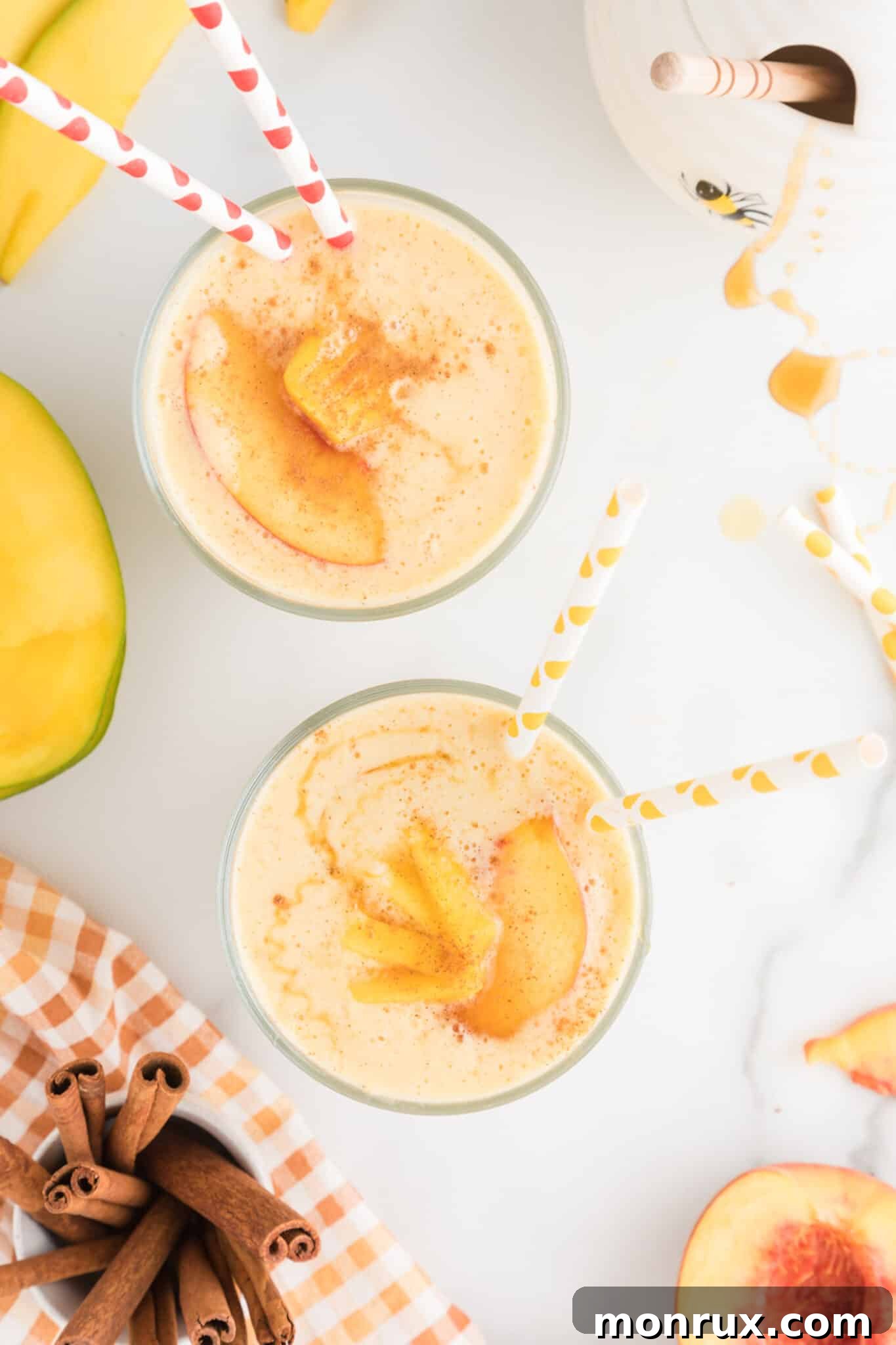 Two vibrant glasses of mango peach smoothie with colorful straws, showcasing its refreshing appeal.
