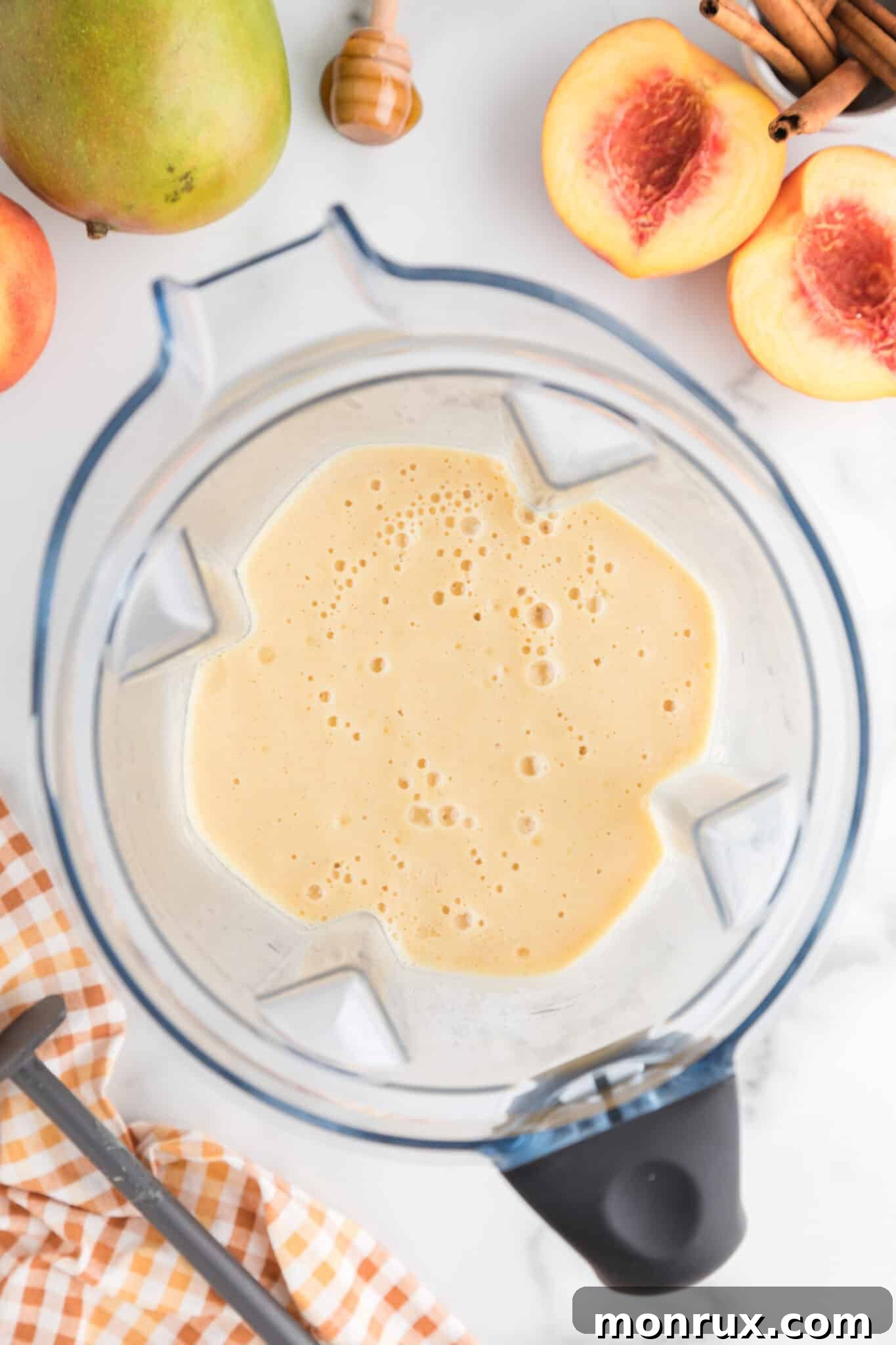 The blended mango peach smoothie swirls beautifully inside the blender, showcasing its smooth, creamy texture and vibrant color.