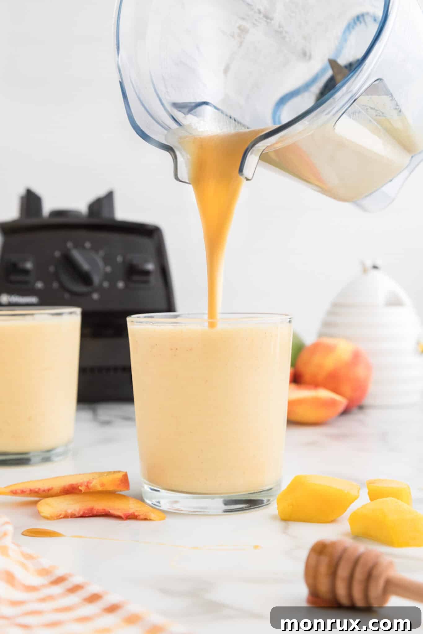The rich, golden mango peach smoothie is being poured gracefully from the blender into a tall glass, ready for enjoyment.