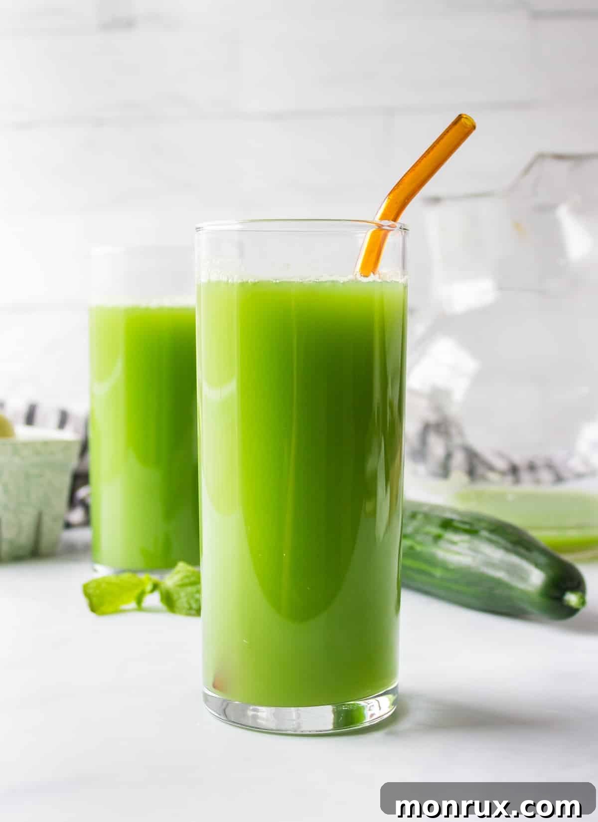 A tall glass of vibrant green cucumber juice with a straw, placed on a clean kitchen countertop, ready to be enjoyed.