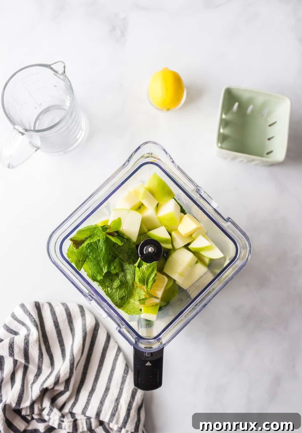 Prepped cucumbers, green apples, lemon, ginger, and mint leaves placed in a blender jar, ready for blending.