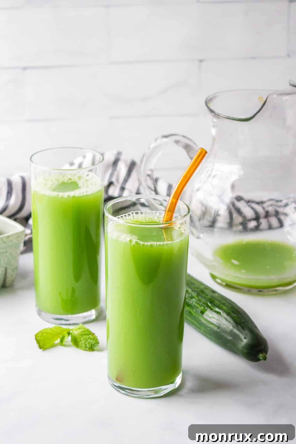 Two glasses of fresh cucumber green juice garnished with cucumber slices, ready to be served.