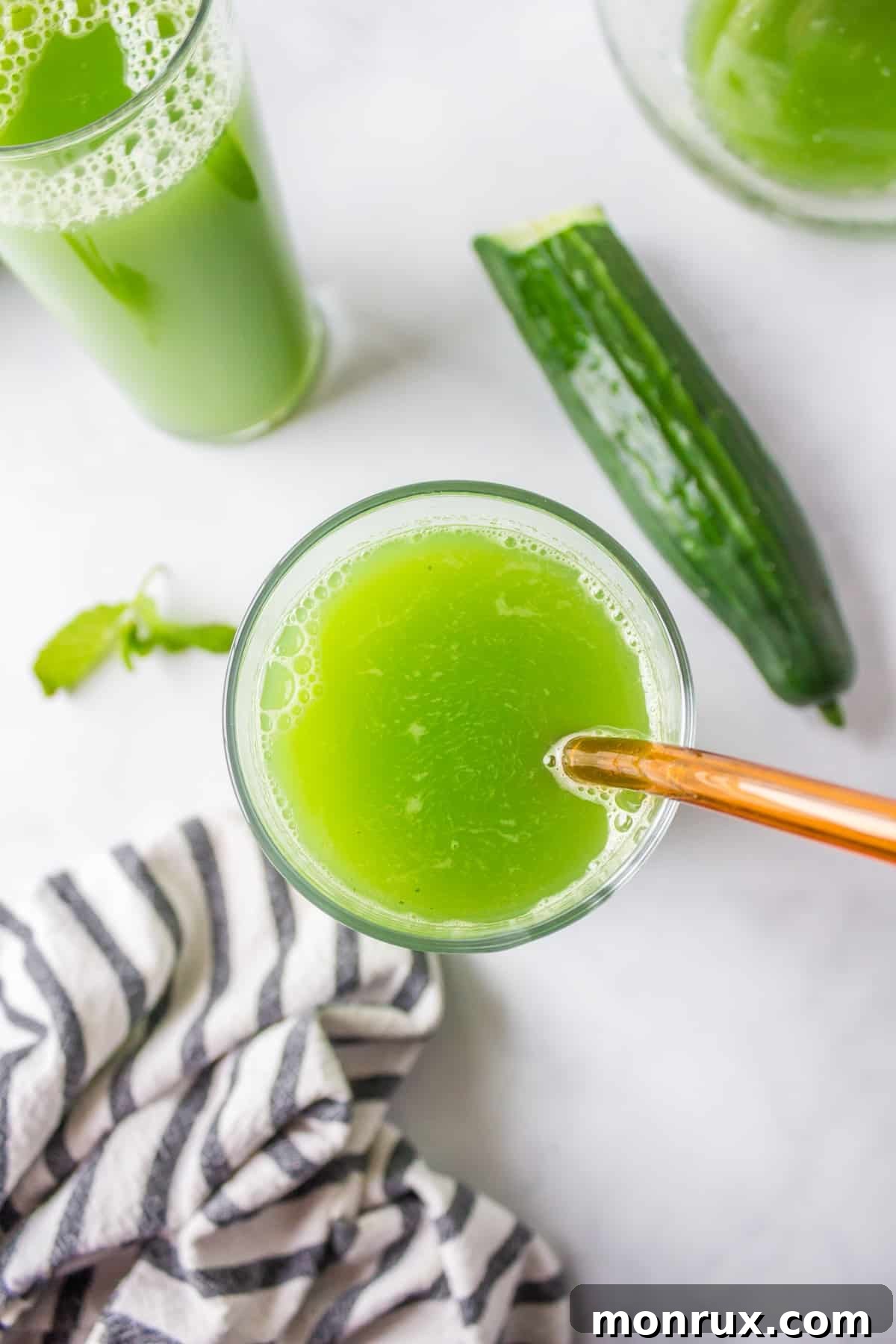 A close-up of a glass filled with bright green cucumber juice and a straw, showcasing its refreshing quality.