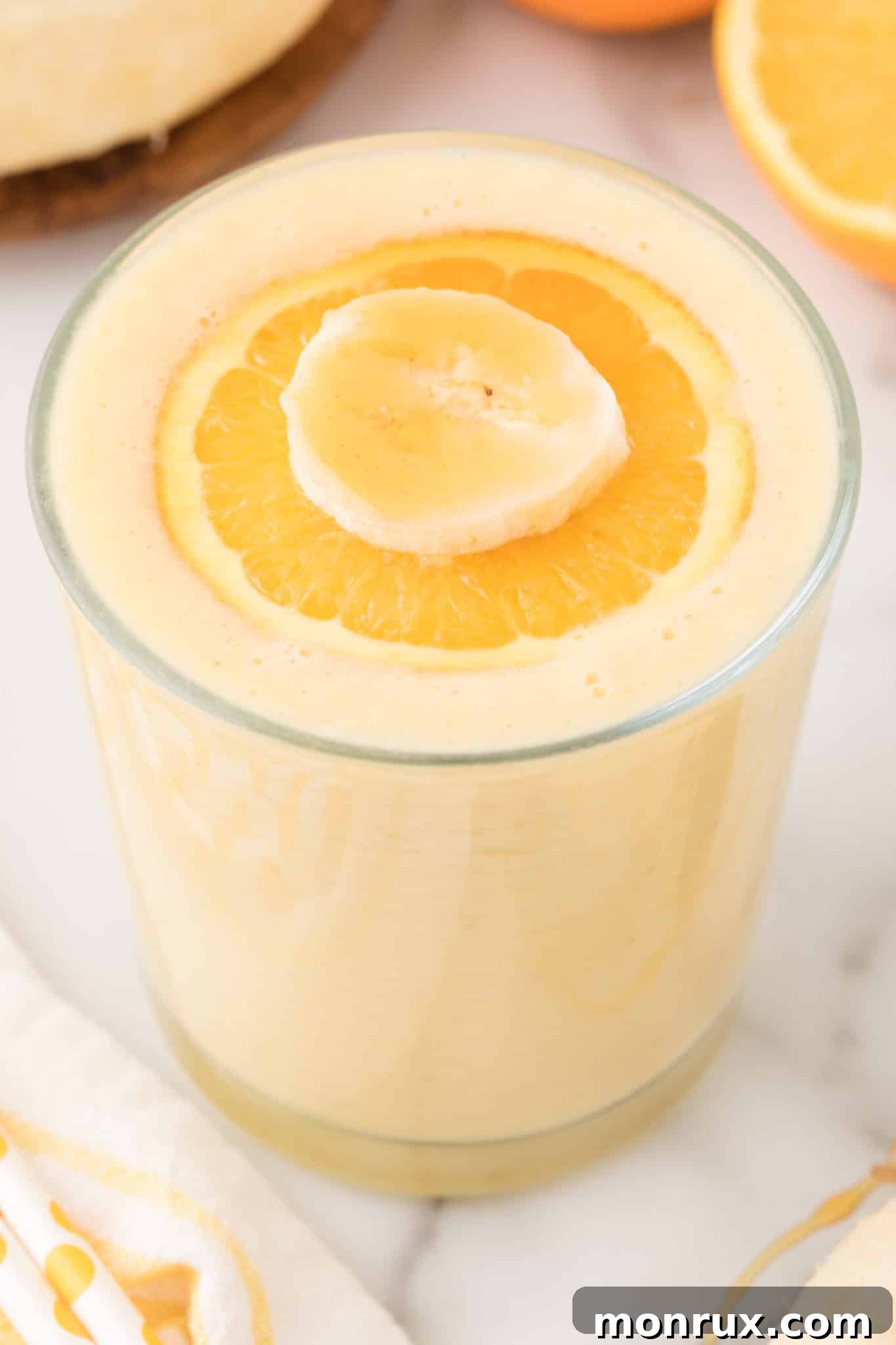 A vibrant orange banana smoothie in a glass, garnished with a fresh orange slice, showcasing its bright and refreshing appeal.