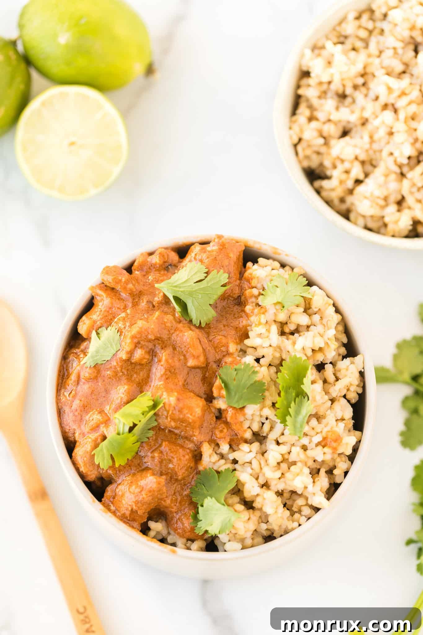 Instant Pot peanut chicken served in a white bowl with brown rice and topped with fresh cilantro leaves.