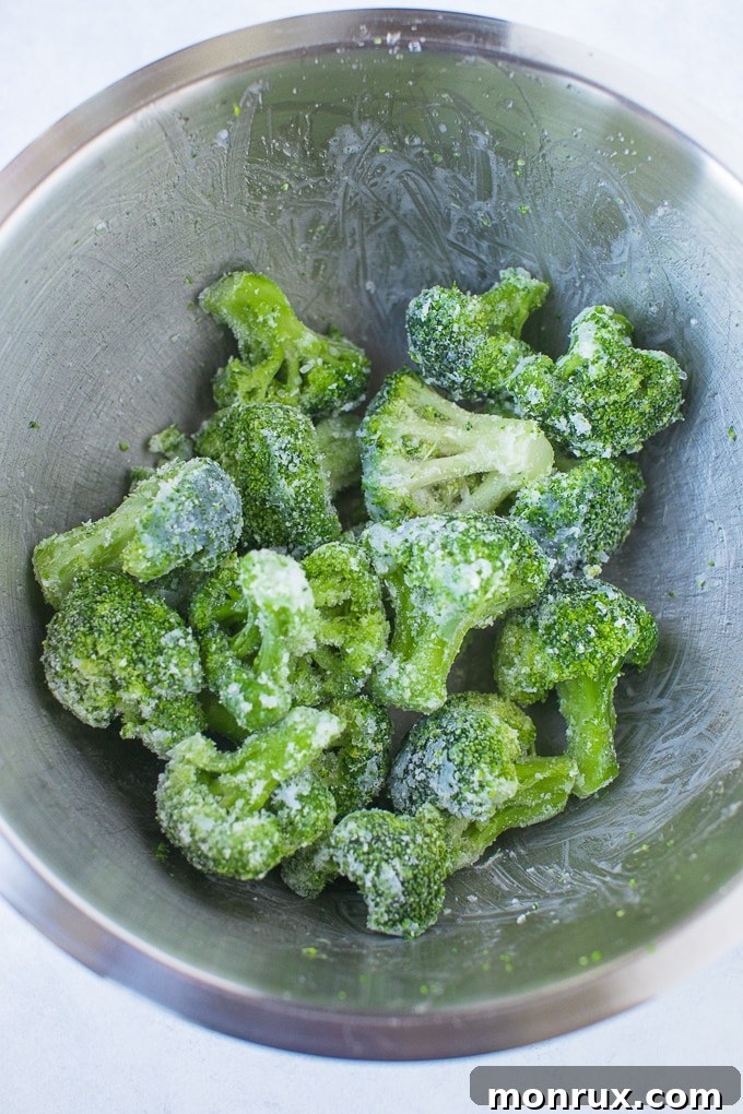 Frozen broccoli florets coated in oil and seasoning in a mixing bowl.