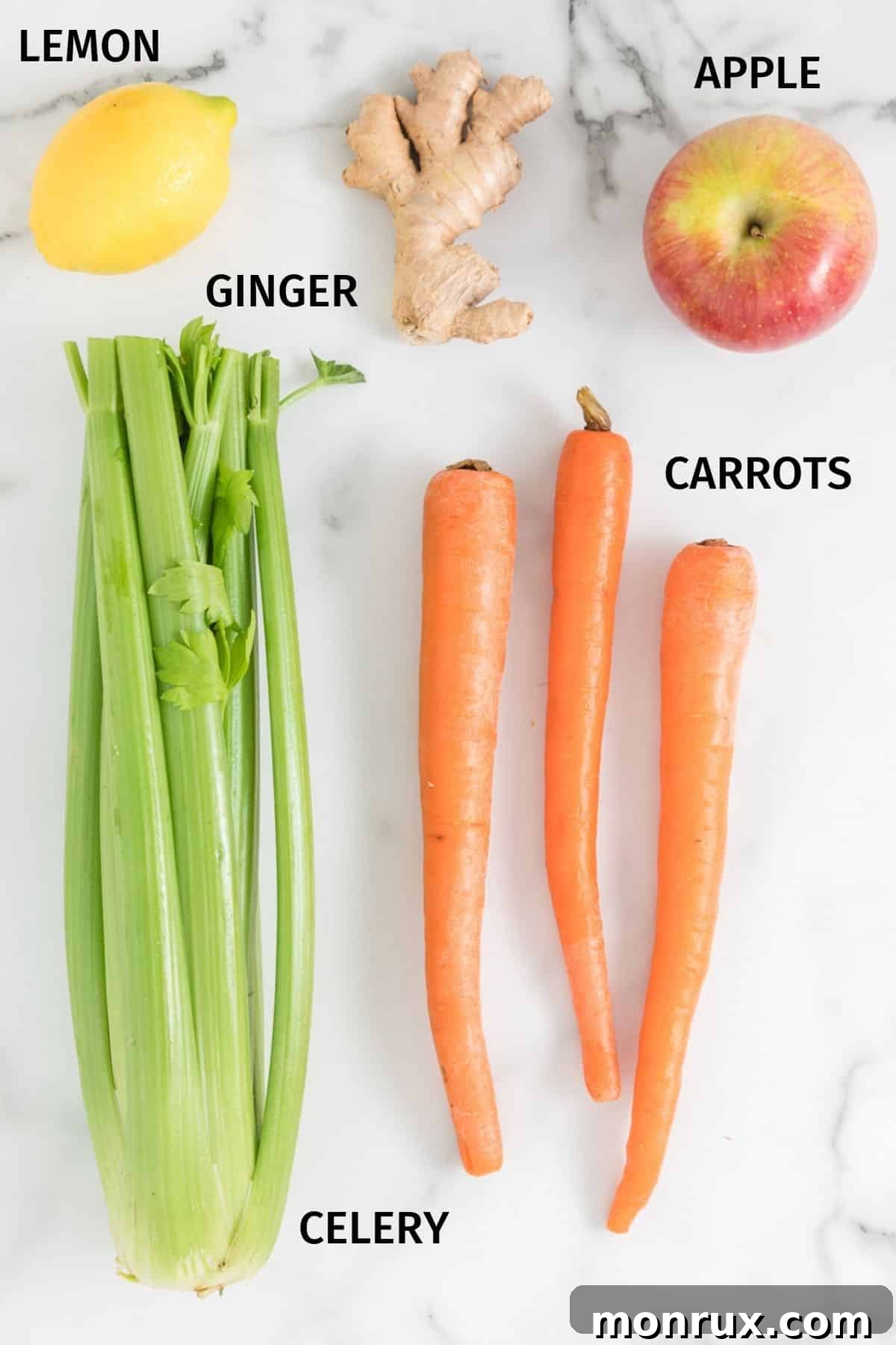 Fresh ingredients for making carrot celery juice, including carrots, celery, apples, ginger, and lemon, arranged on a white surface.