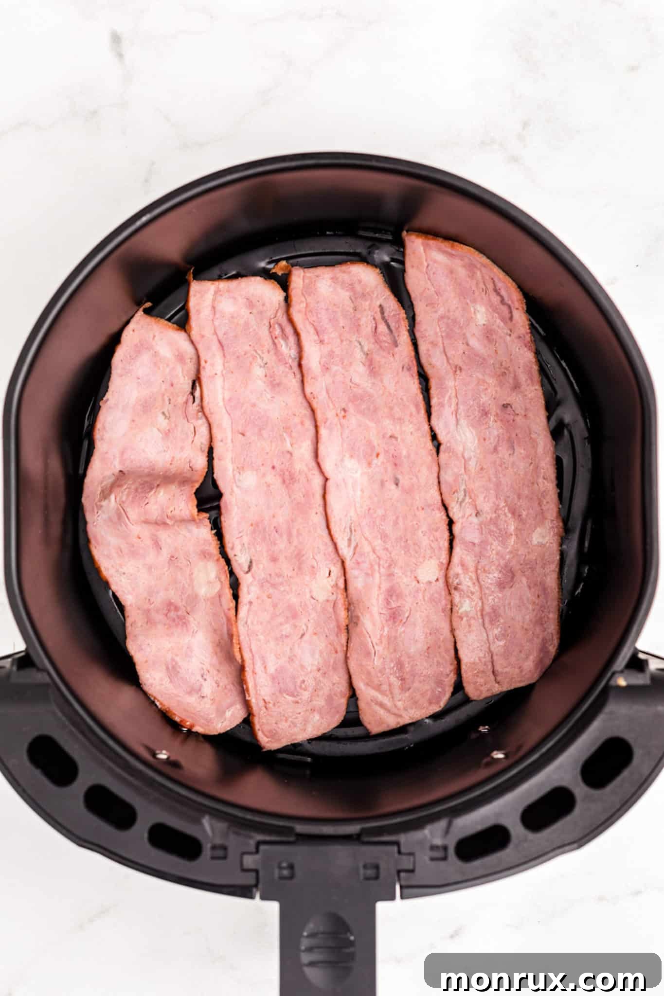 Raw turkey bacon slices arranged in a single layer inside an air fryer basket.