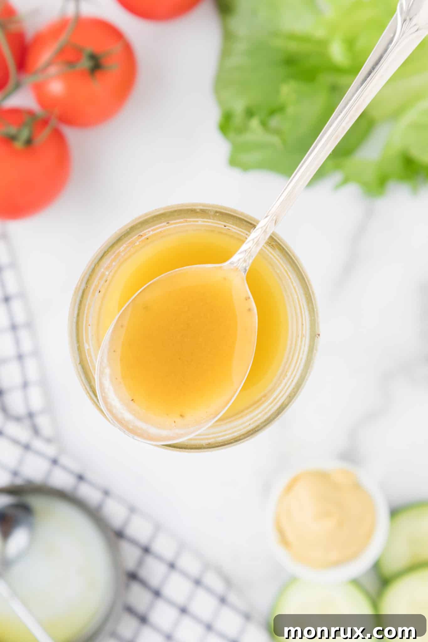 A close-up shot of a spoonful of creamy honey mustard dressing, artfully presented on a wooden table alongside fresh tomatoes and crisp lettuce leaves.