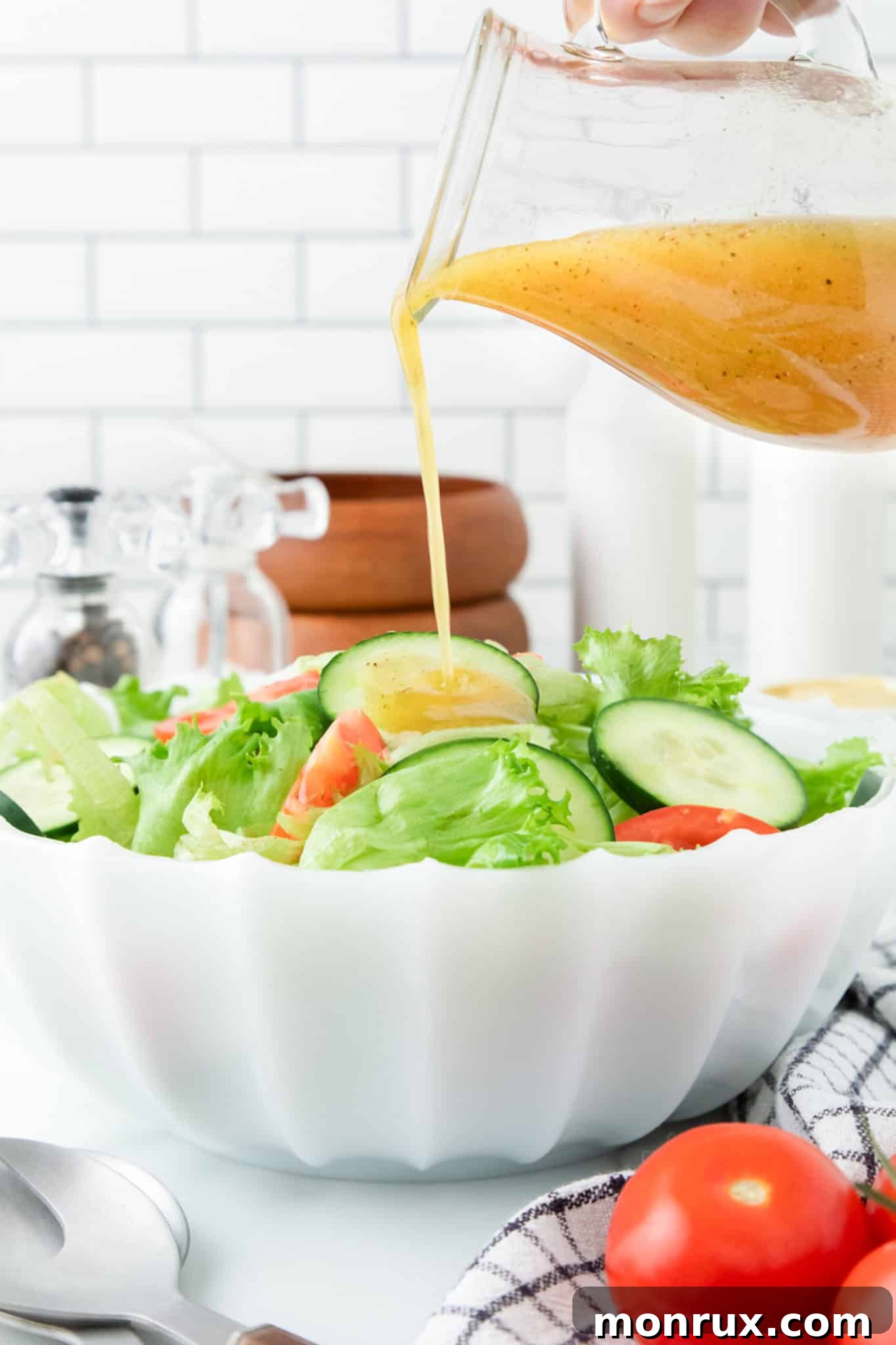 A hand pouring golden honey mustard vinaigrette onto a vibrant green salad, showcasing its perfect consistency.