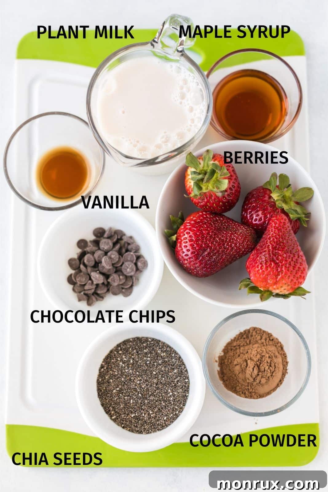 A selection of fresh ingredients including chia seeds, almond milk, cocoa powder, strawberries, and maple syrup laid out on a table.