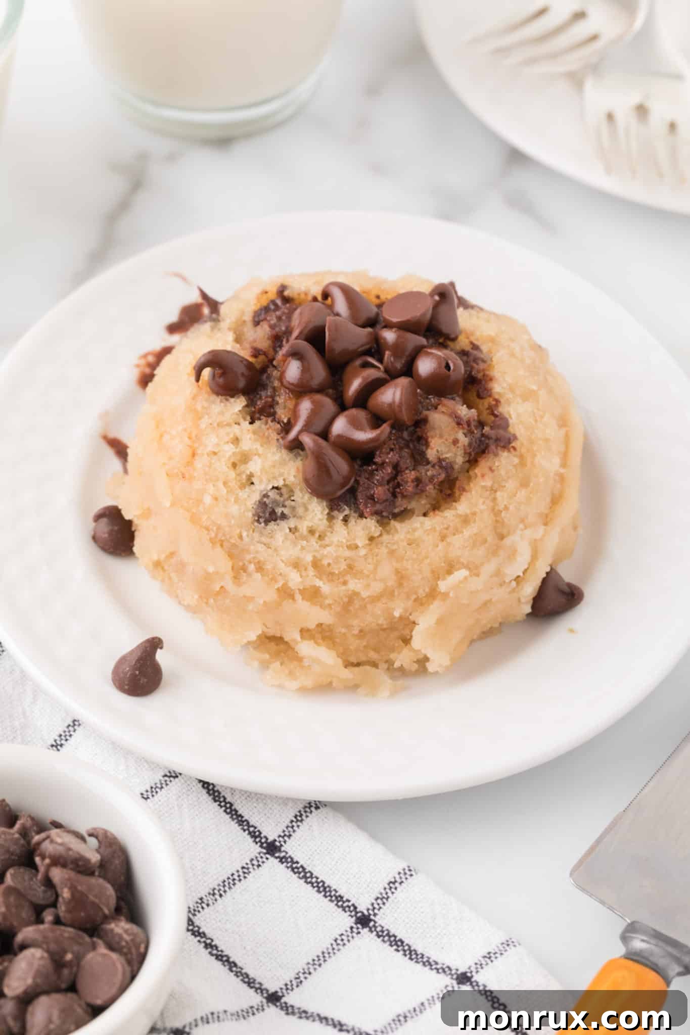 A warm, fluffy vegan chocolate chip mug cake, served on a plate and topped with extra chocolate chips.