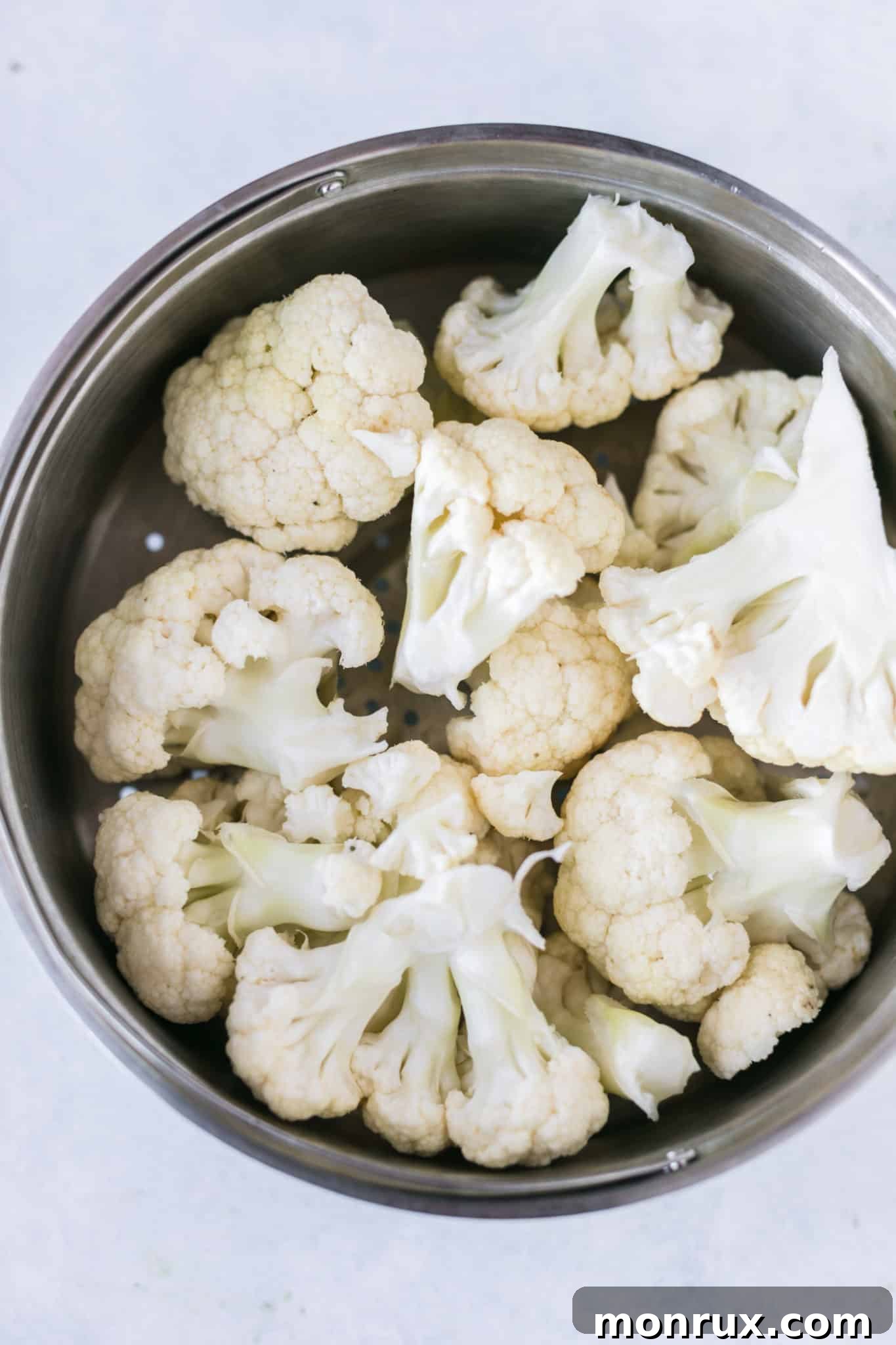 Freshly cut cauliflower florets are neatly arranged within a metal steamer basket, ready for cooking.