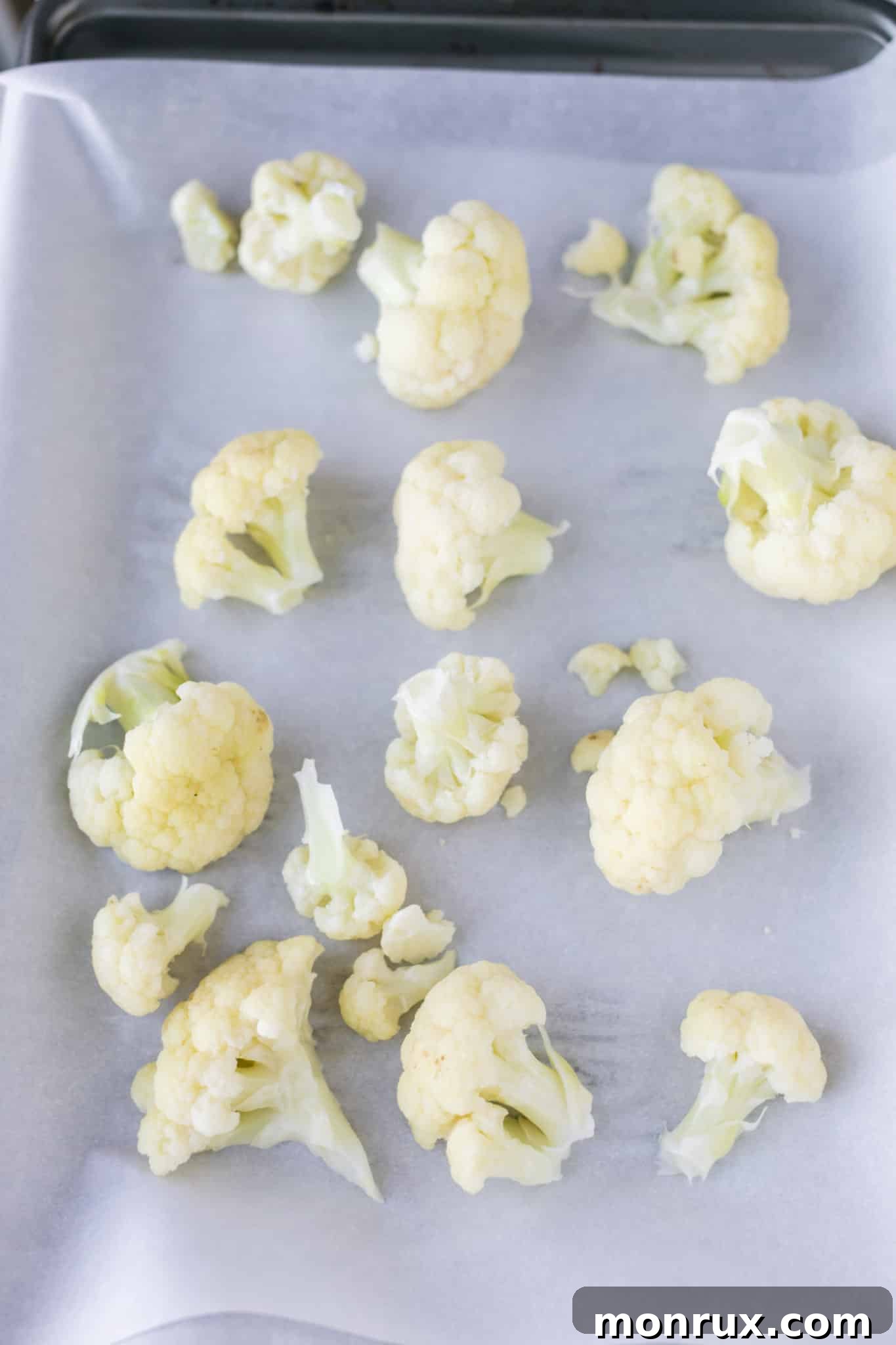 Blanched and cooled cauliflower florets are spread out in a single layer on a baking sheet lined with parchment paper, preparing for flash freezing.
