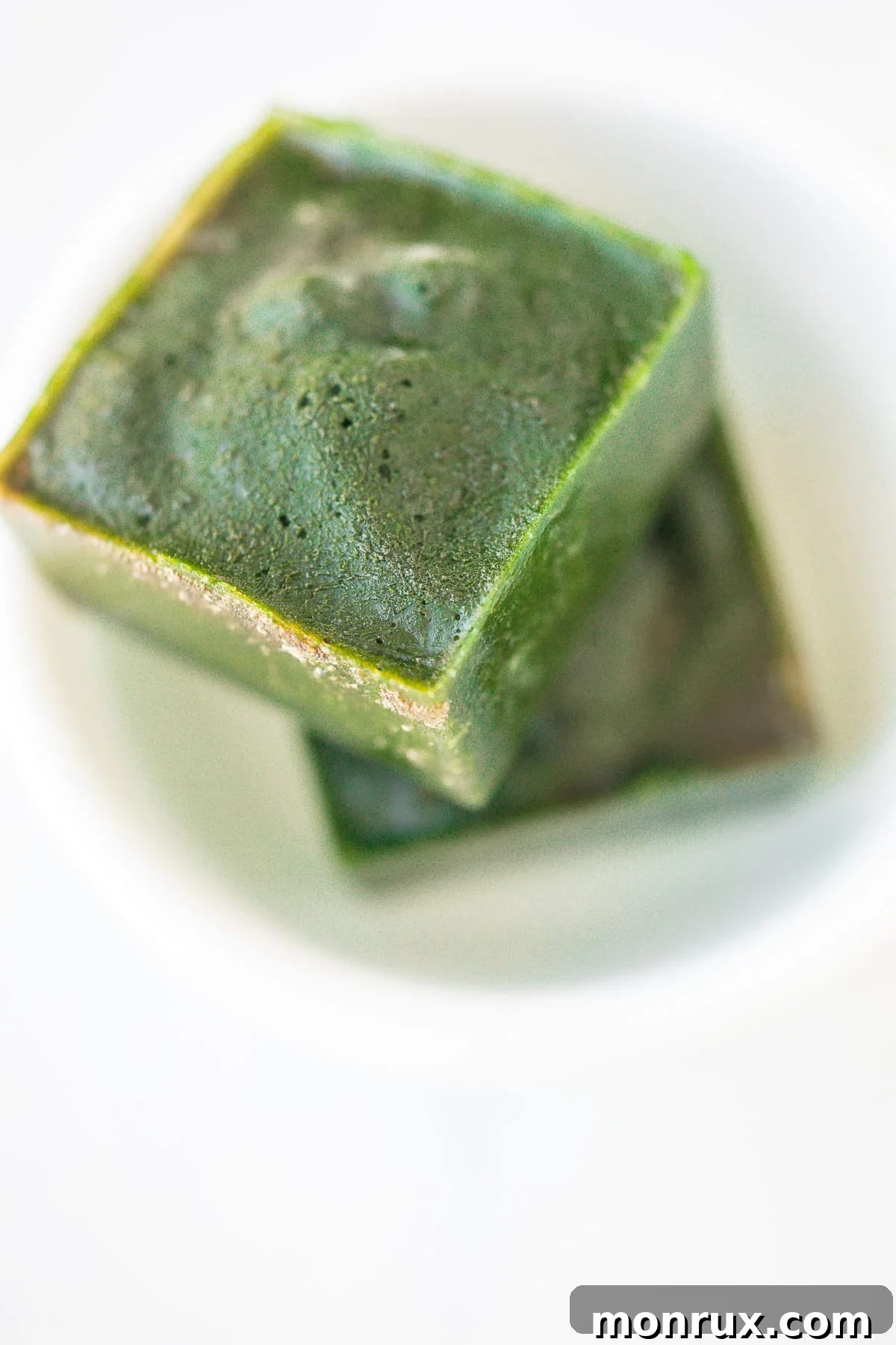 Two spinach ice cubes in a white bowl, ready for use