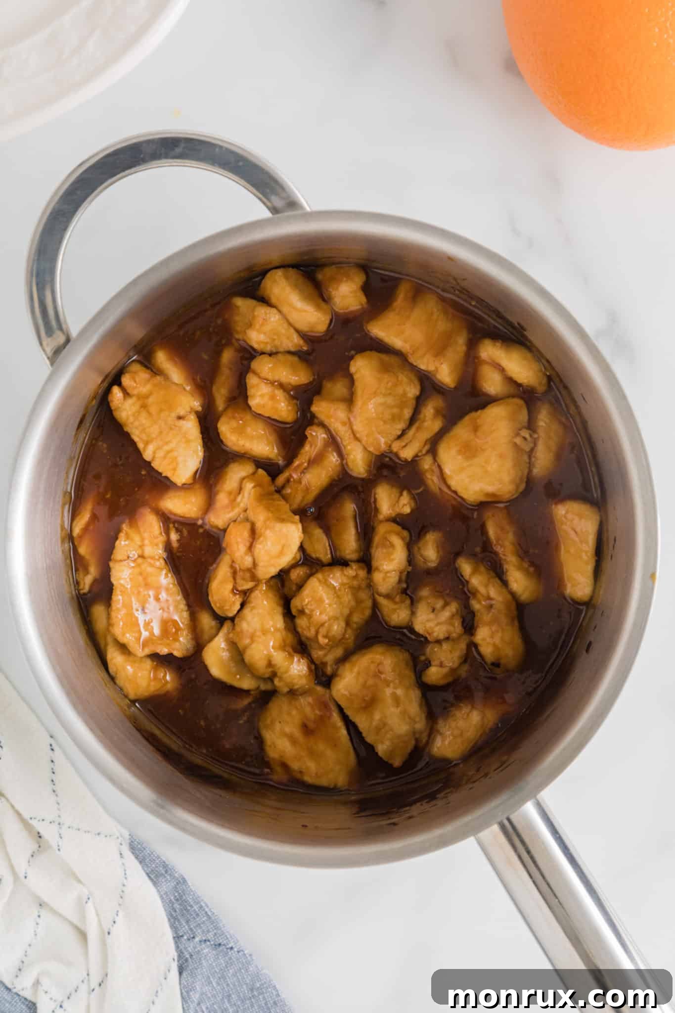 Cooked chicken breast chunks in a saucepan of orange sauce.