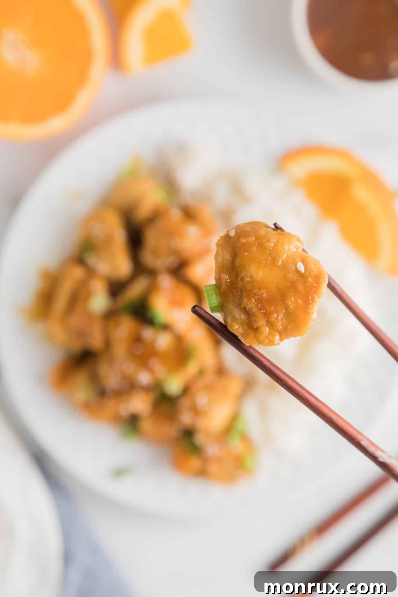 Chopsticks holding up a single bite of air fryer orange chicken.
