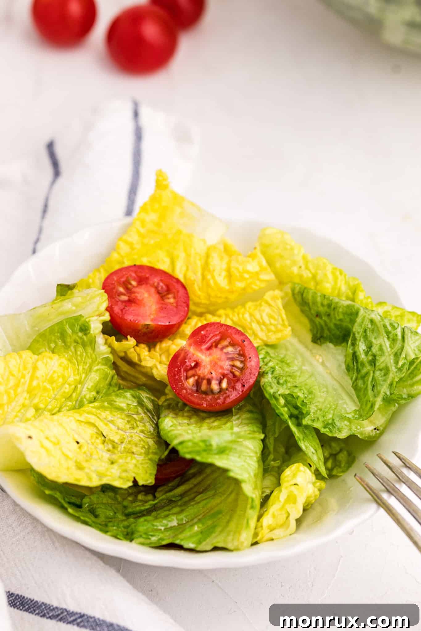 A serving of romaine salad adorned with vibrant cherry tomatoes, presented on a white plate.