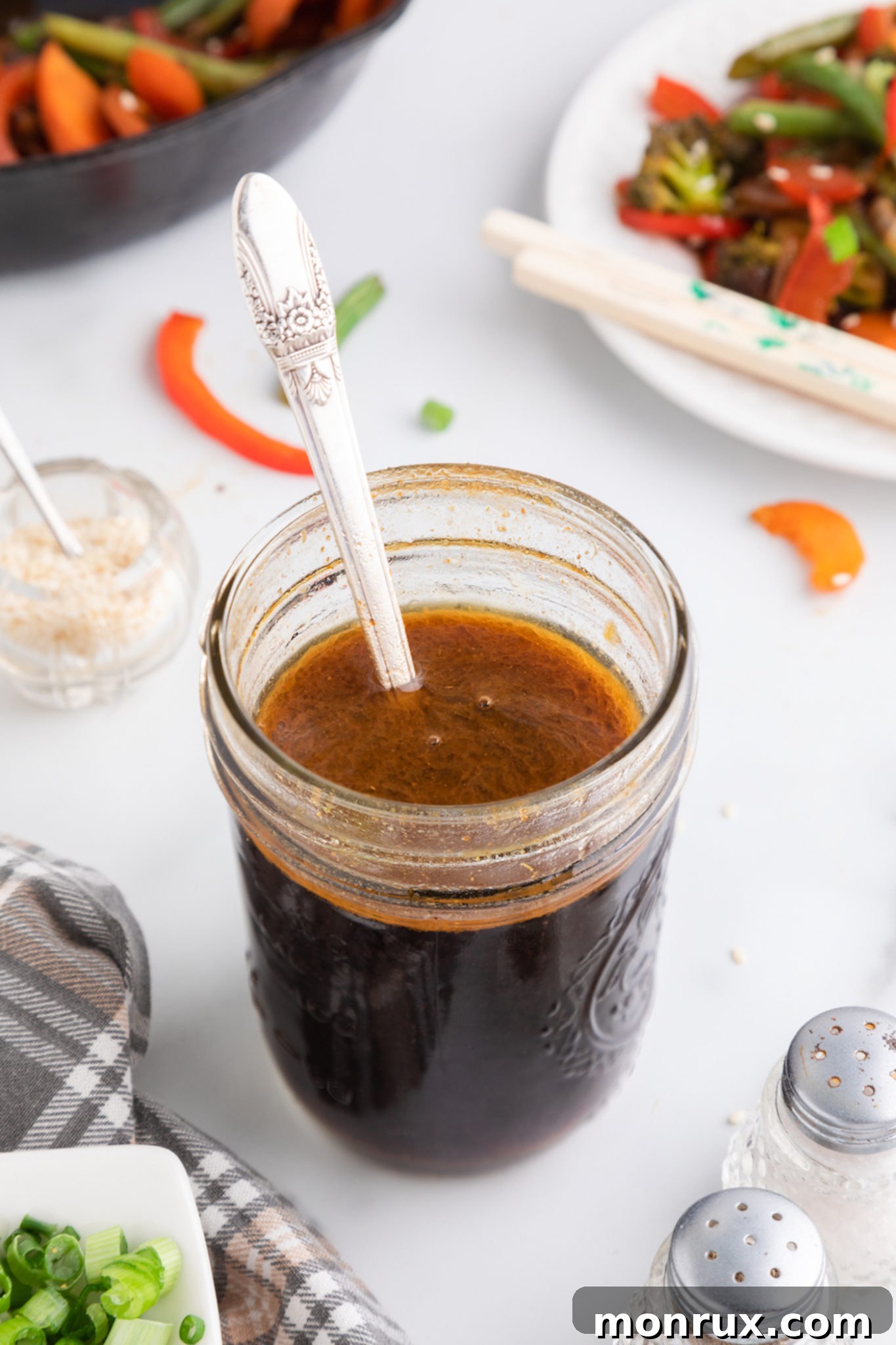 A silver spoon in a jar of freshly made stir fry sauce, highlighting its rich texture and appetizing color.