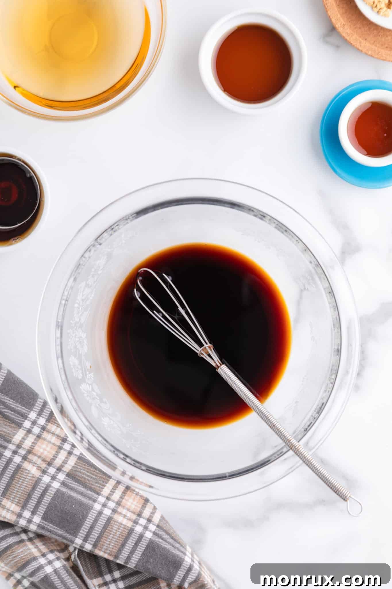 A small silver whisk in a glass bowl of soy sauce, illustrating the initial mixing step for the stir-fry sauce.