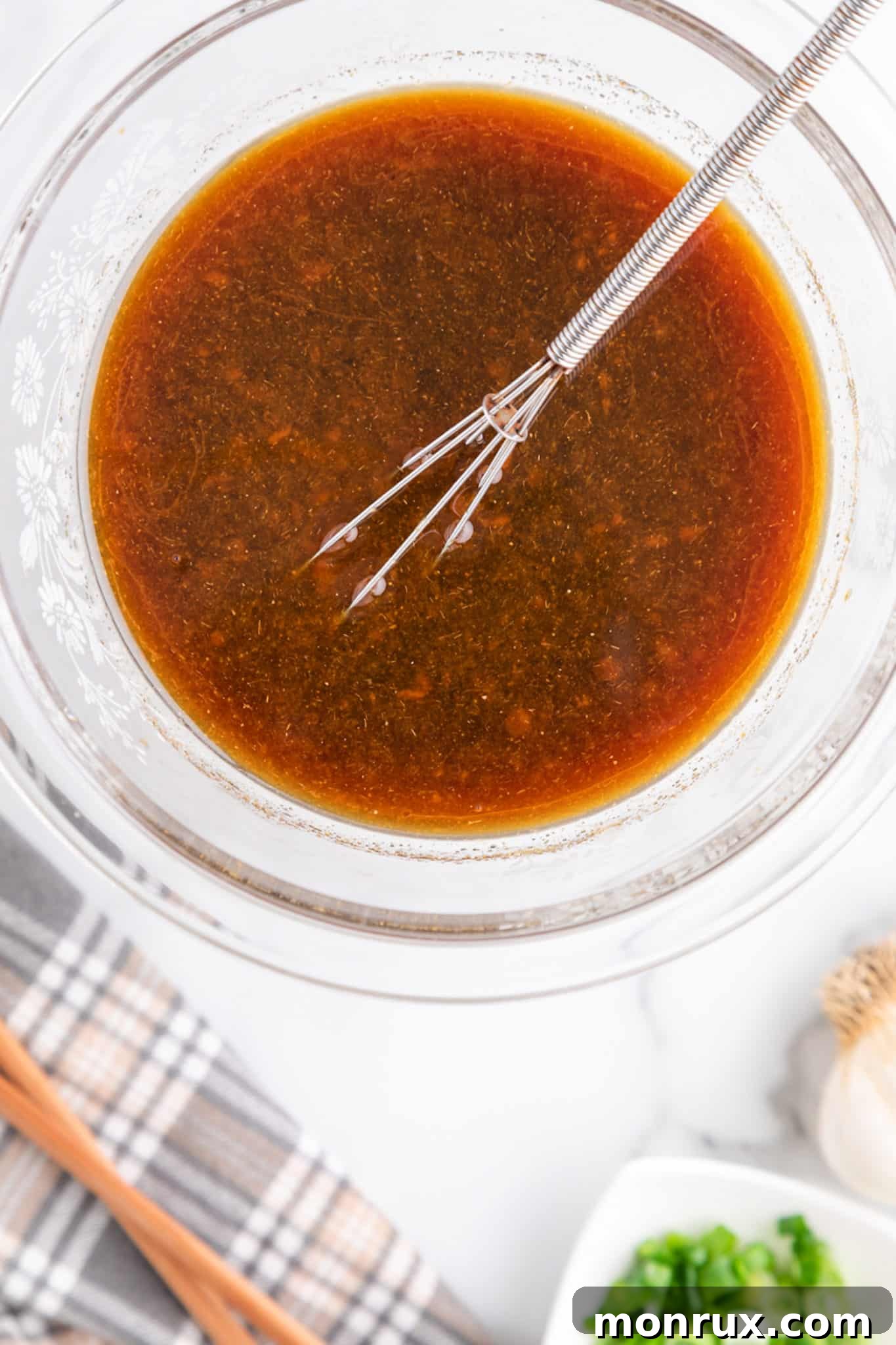 A whisk in a clear glass bowl of stir fry sauce, demonstrating the complete mixing process and smooth consistency.