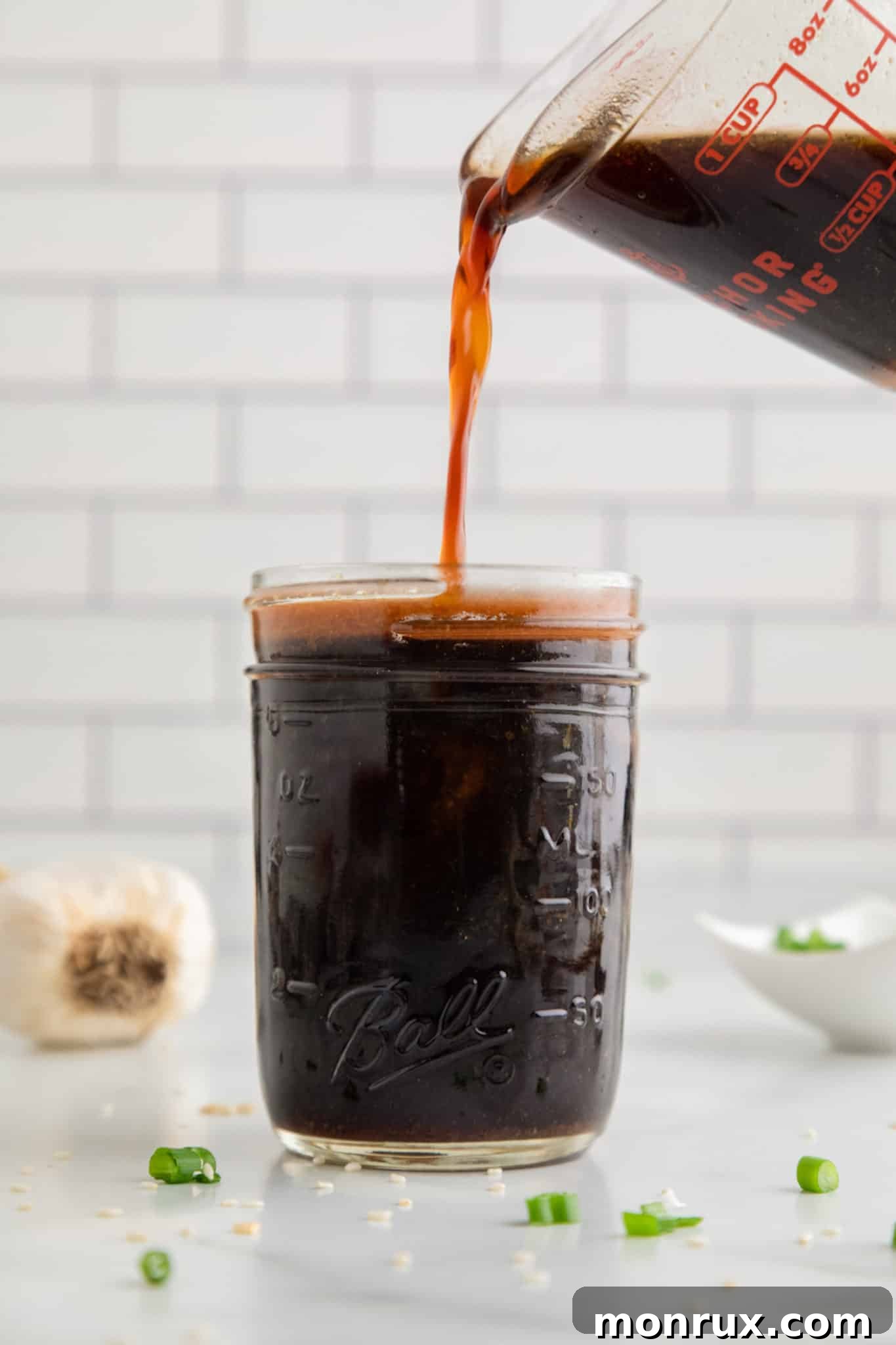 A glass measuring cup pouring stir fry sauce into a mason jar for storage.