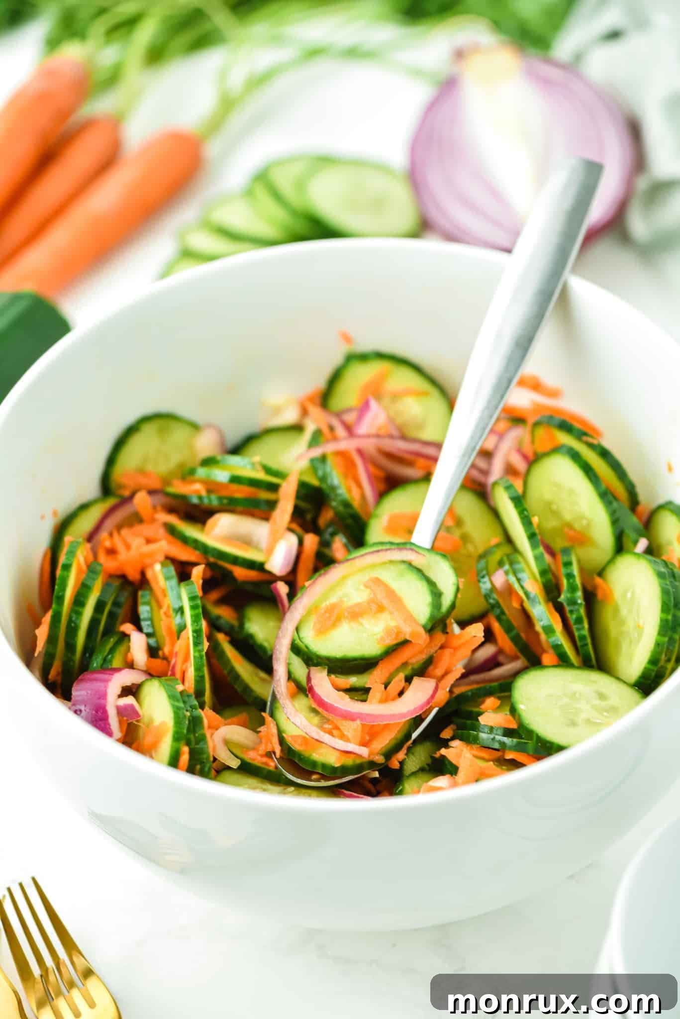 A forkful of crisp carrot and cucumber salad, artfully arranged over a small white bowl brimming with the refreshing mix.