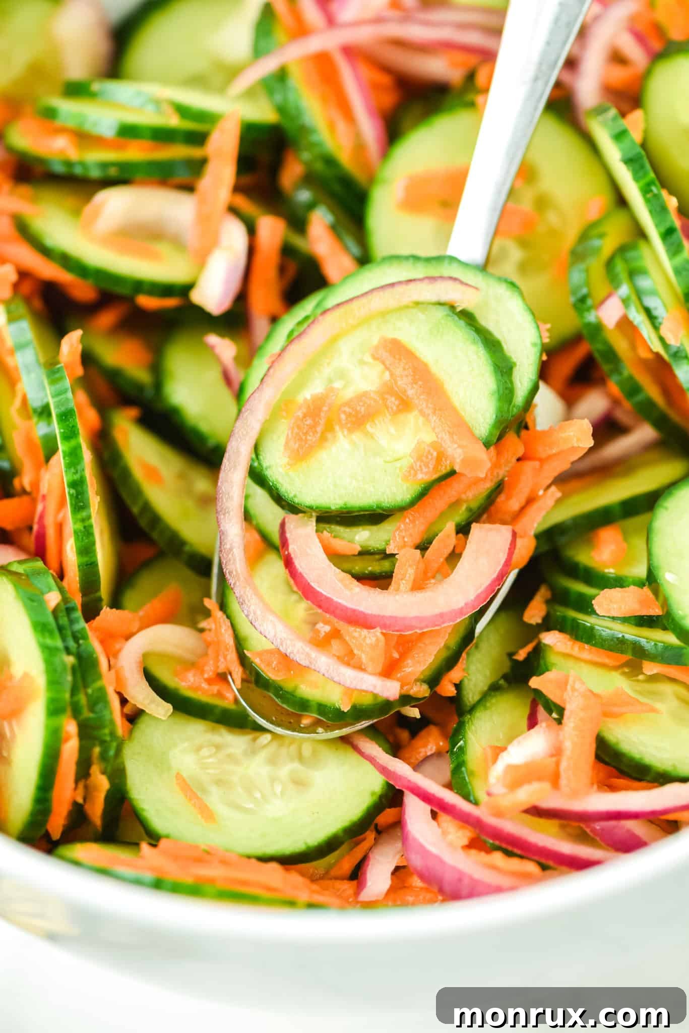 A serving of crisp cucumber carrot salad on a fork, held just above the main serving bowl, ready to be enjoyed.