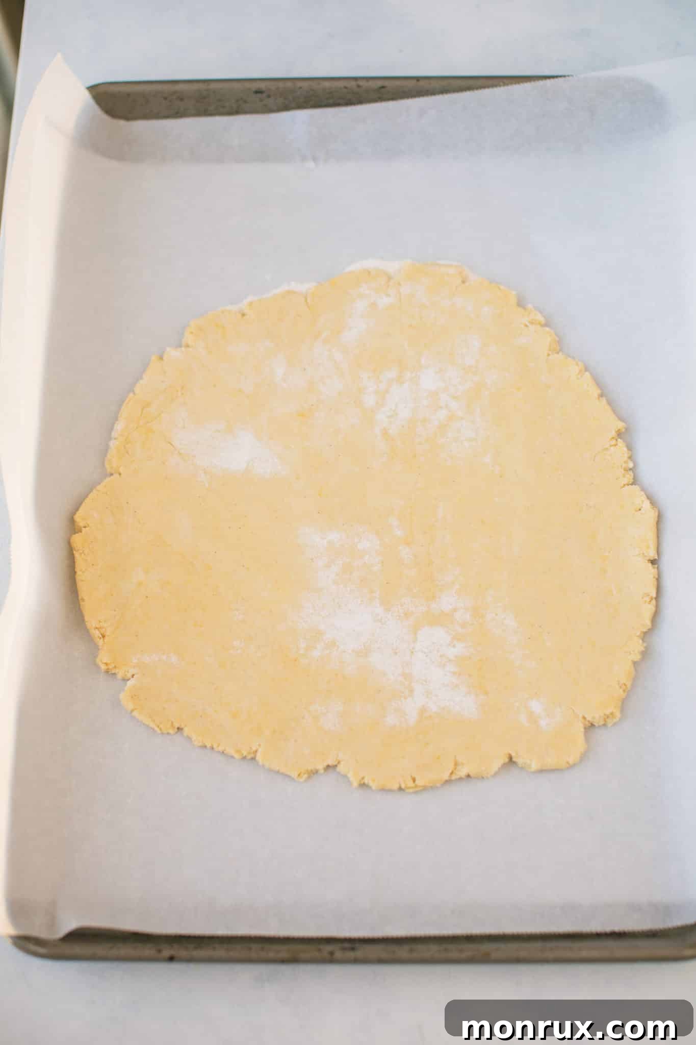 Cassava pizza crust rolled out thinly on a baking sheet lined with parchment paper.