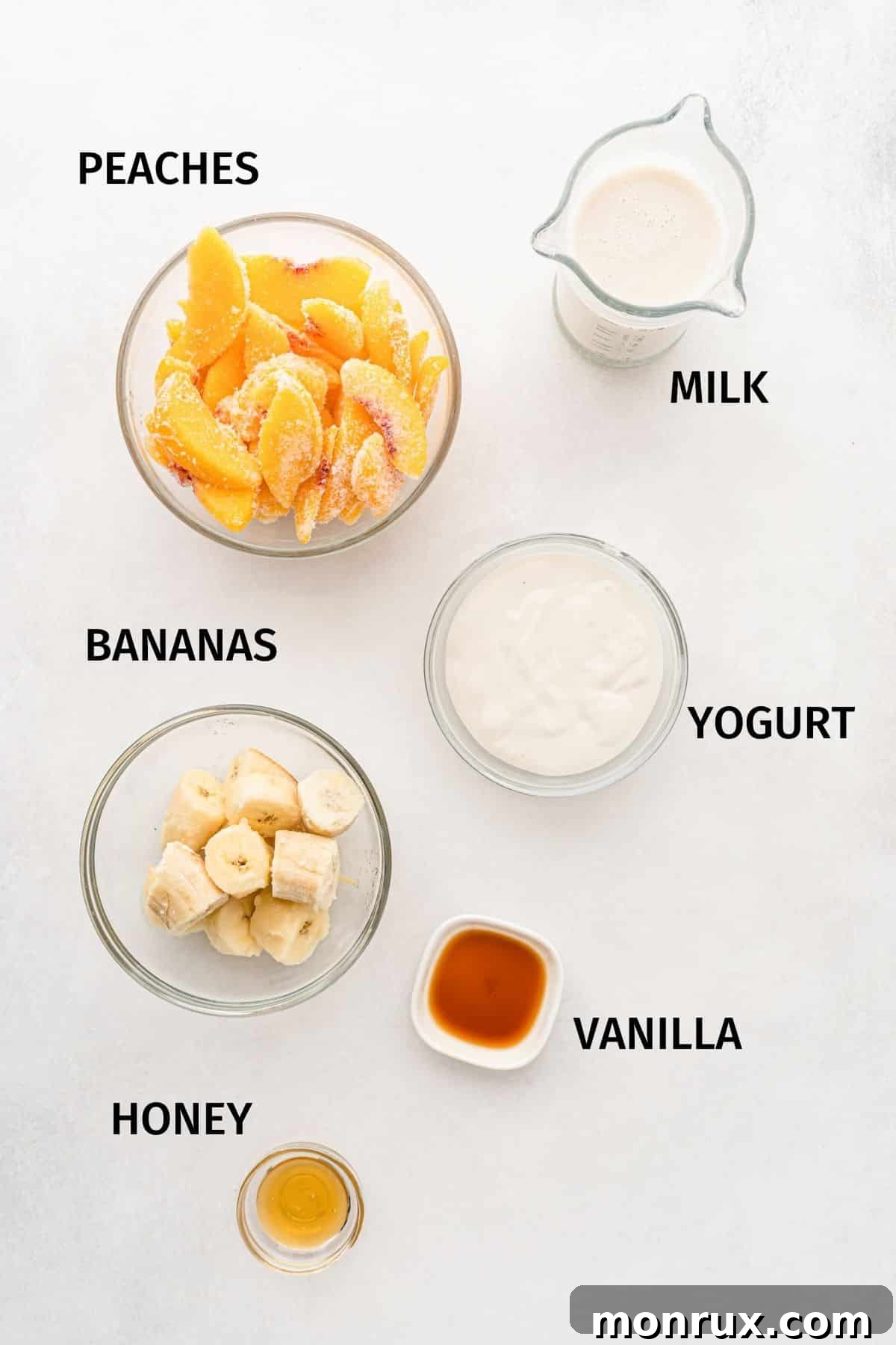 Small bowls with ingredients for a banana peach smoothie, including frozen peaches, banana slices, yogurt, and a liquid on a white surface.