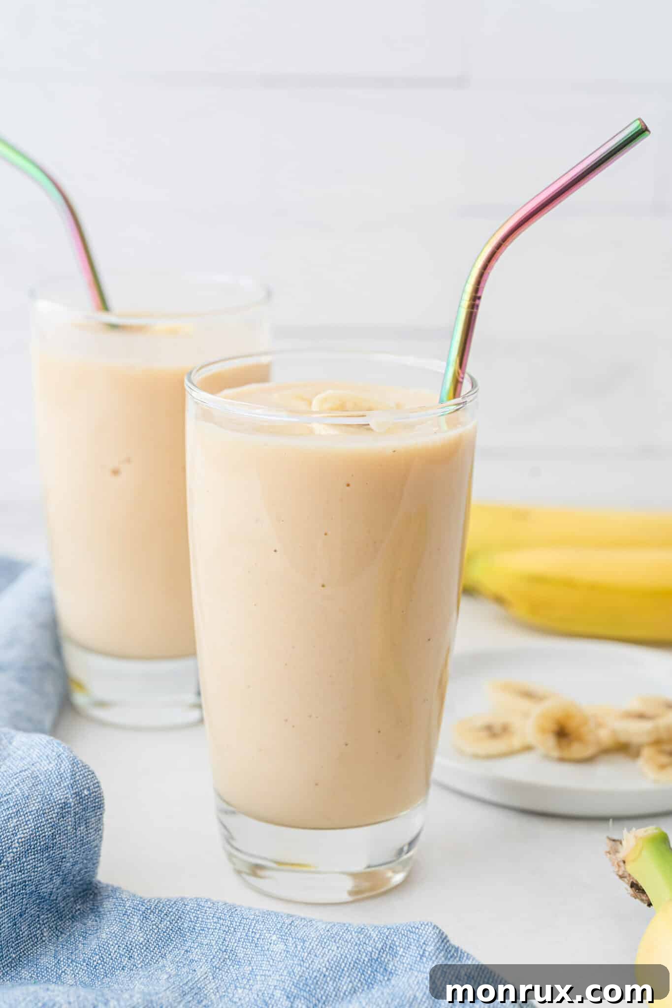 Two glasses of creamy banana peach smoothie with iridescent straws, ready to be enjoyed.