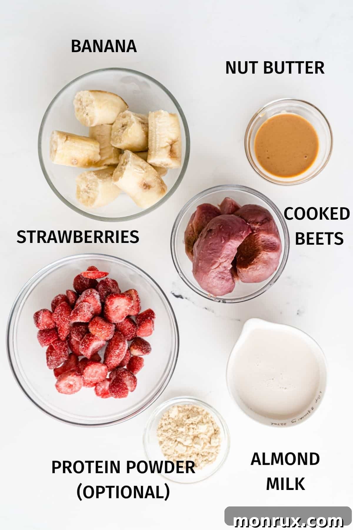A beautiful flat lay of fresh ingredients for a healthy banana beet smoothie, including frozen bananas, strawberries, cooked beets, almond milk, and nut butter.