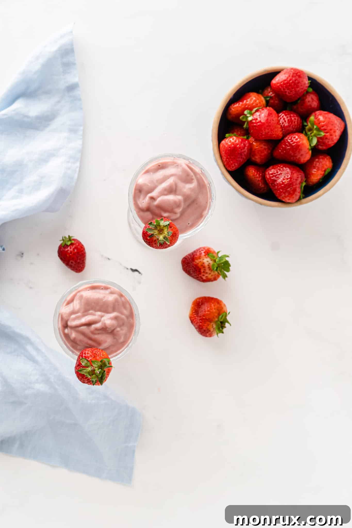 Two glasses of vibrant beet smoothie next to a bowl of fresh strawberries, ready for serving.