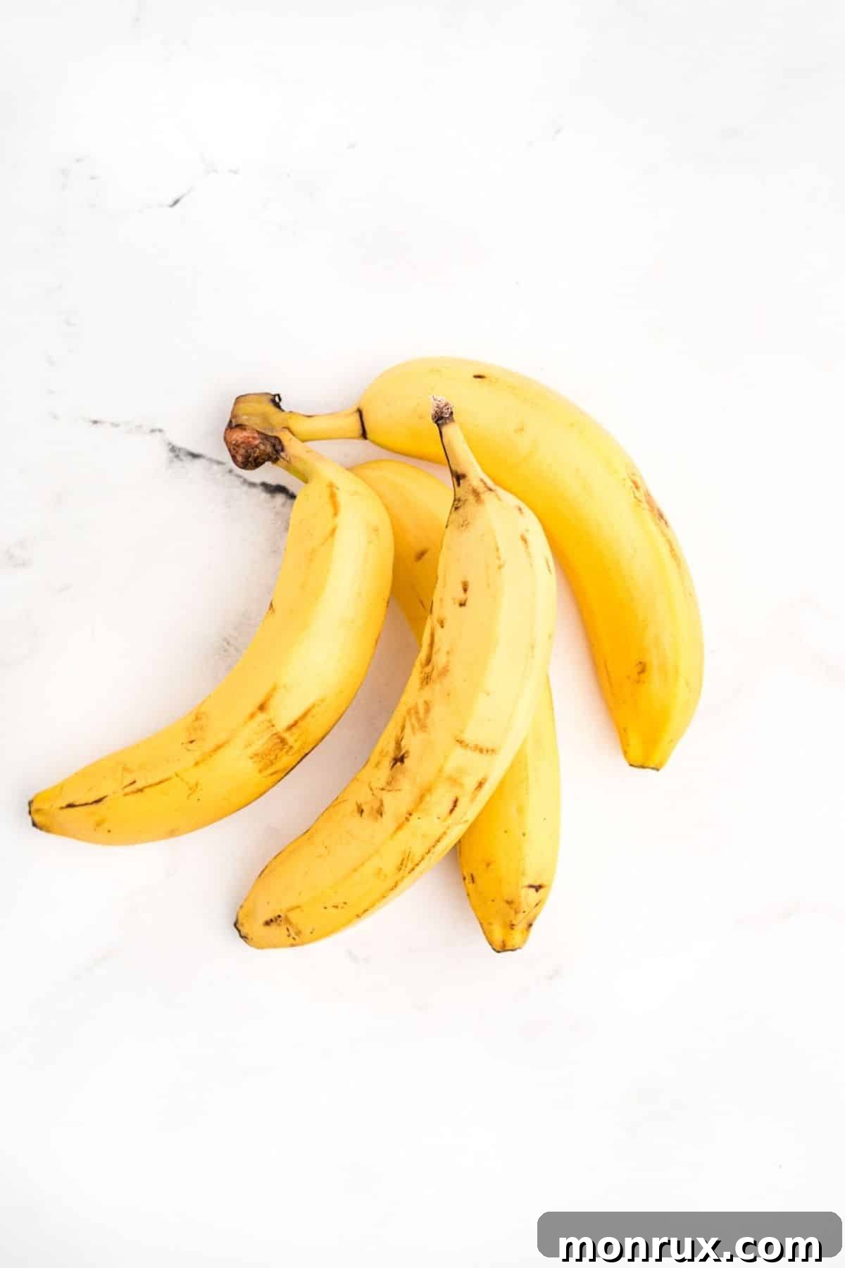Four ripe unpeeled bananas on a white surface.