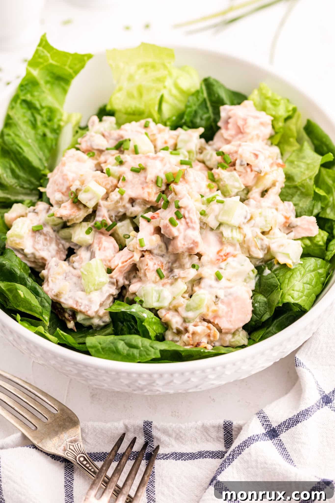 Salmon salad with celery and mayo topping lettuce in a large white bowl.