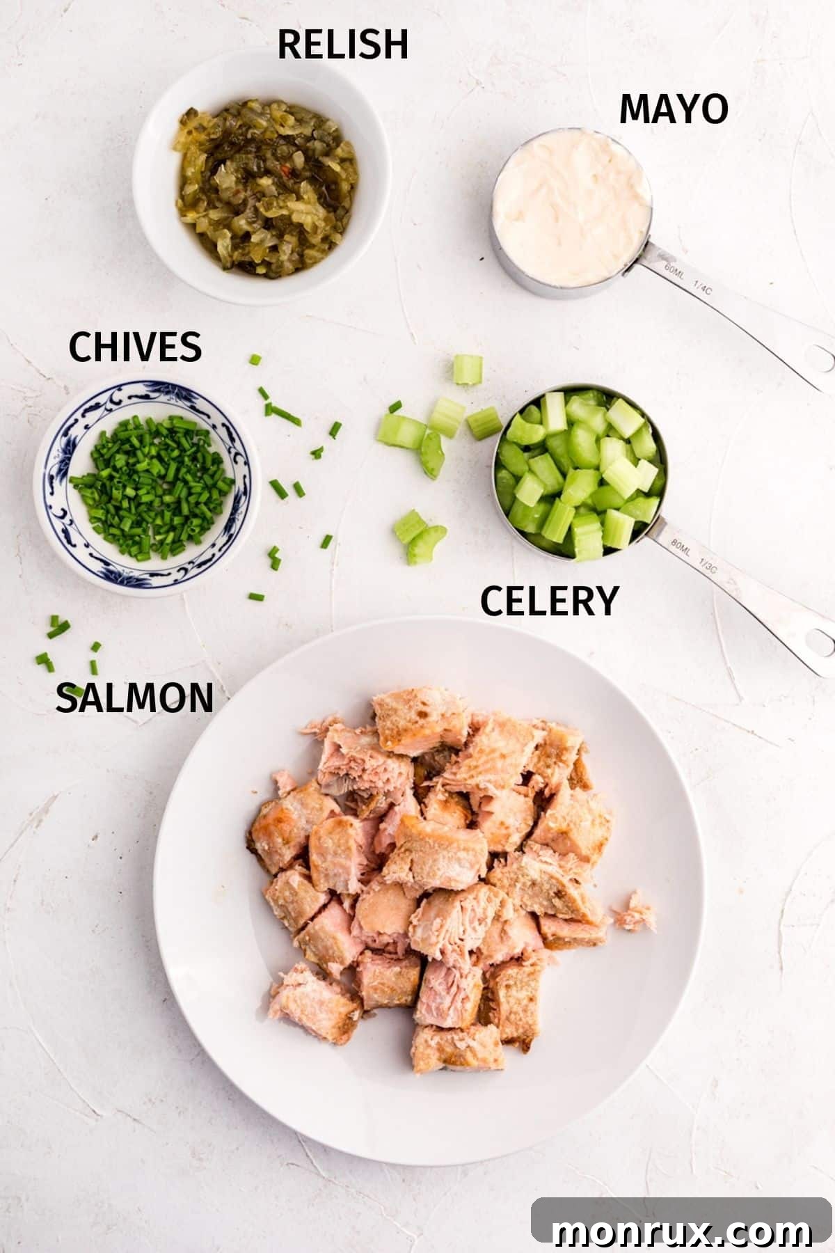 Salmon salad ingredients in small bowls on a white surface.