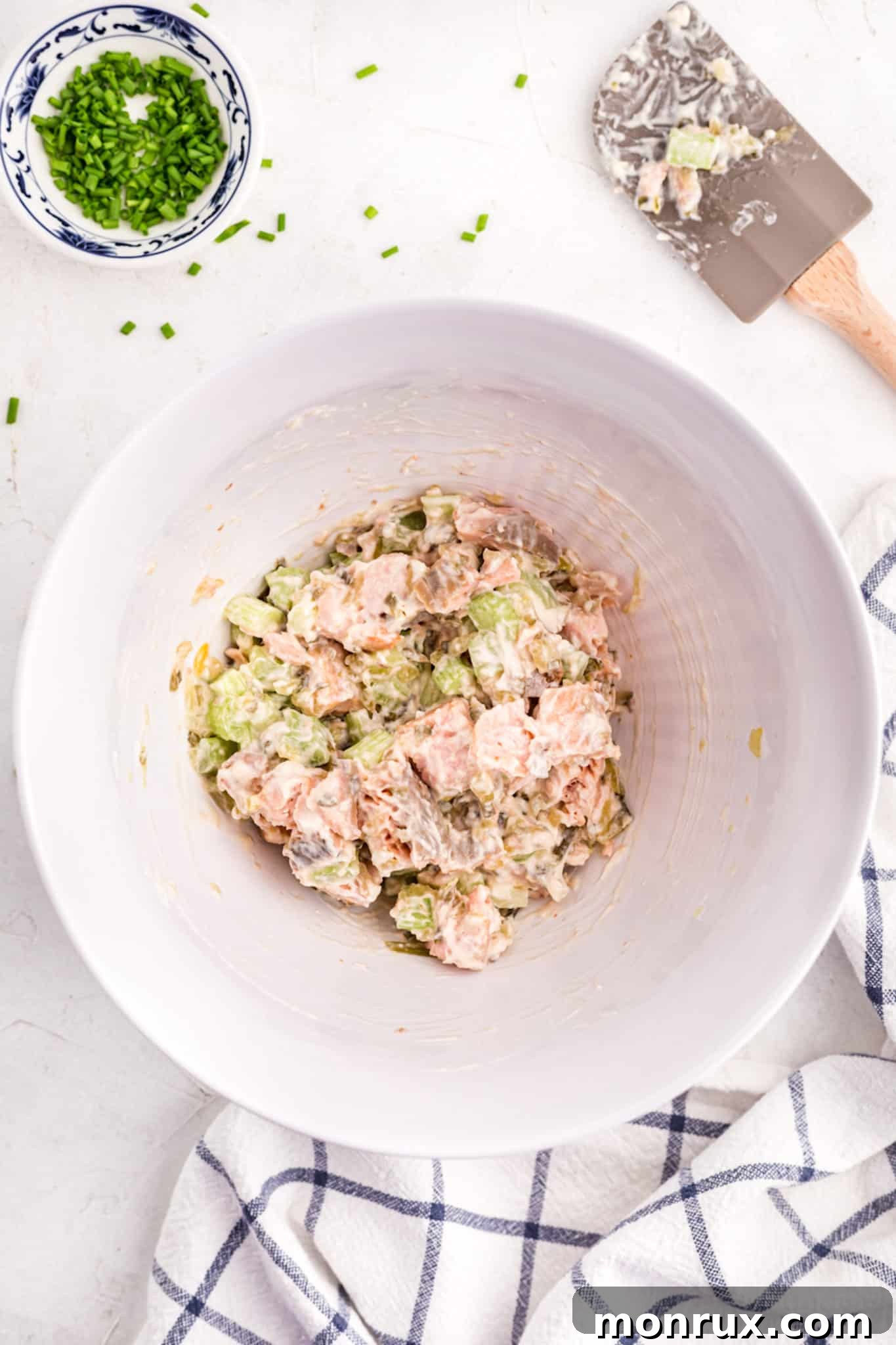 Salmon salad mixed up with mayo in a large white mixing bowl.
