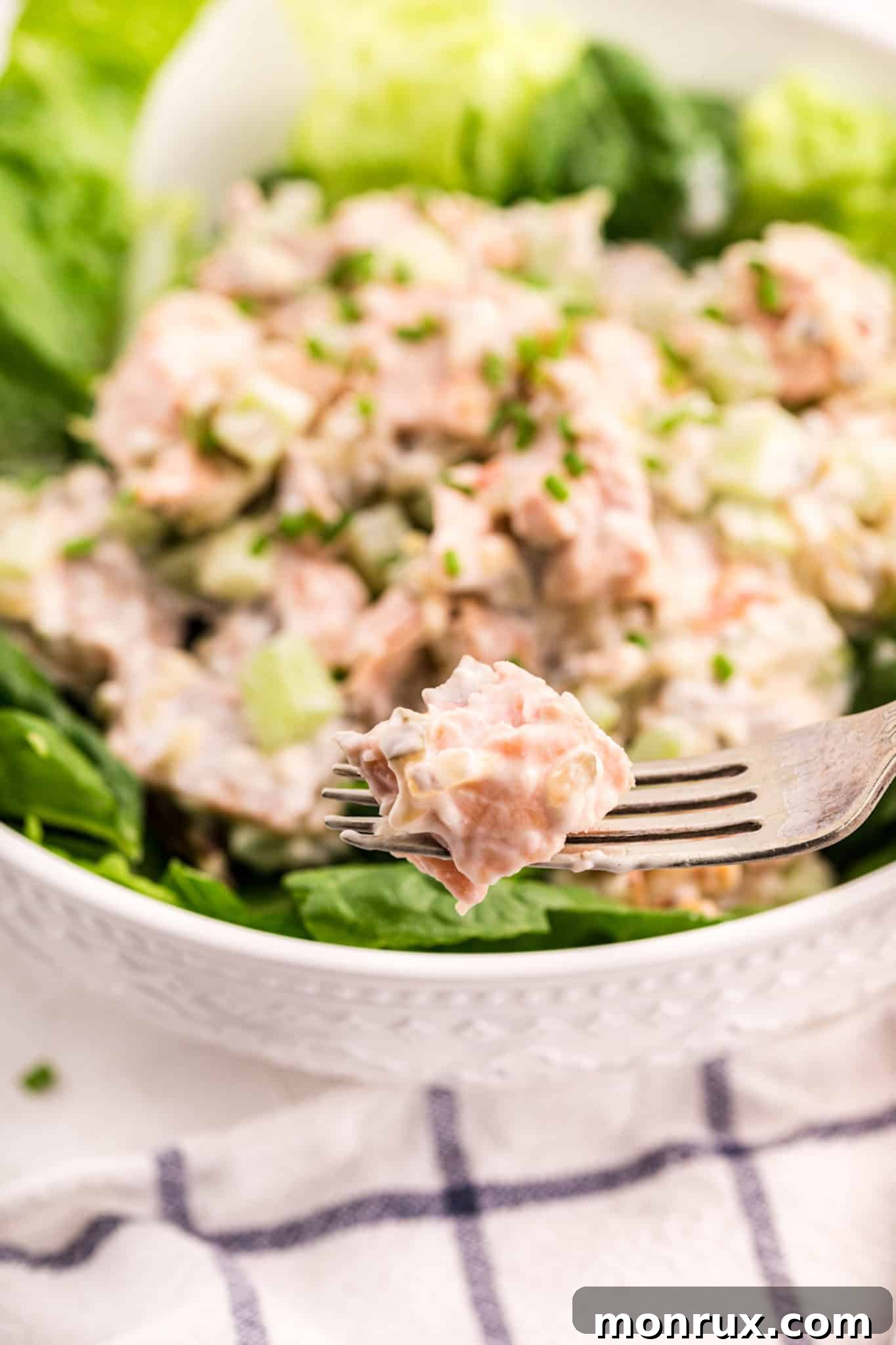A fork holding a bite of salmon salad over a filled bowl.