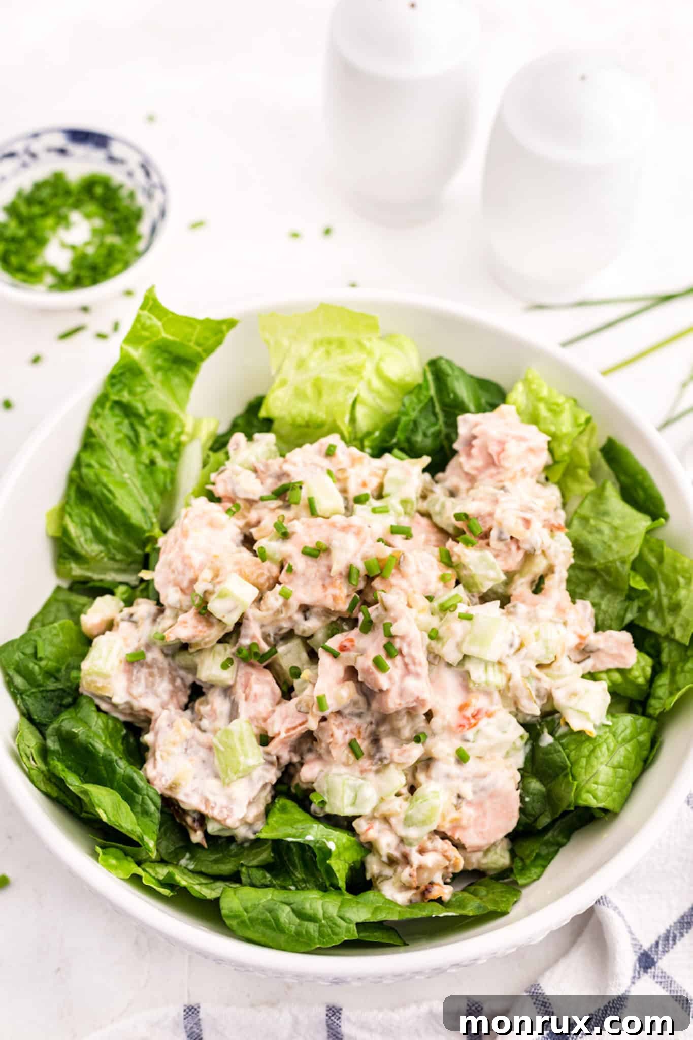 A large white salad bowl filled with greens topped with salmon salad.