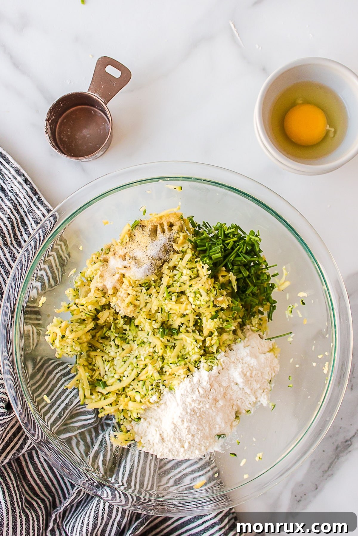 A large mixing bowl filled with grated zucchini and potato, ready for the next ingredients.