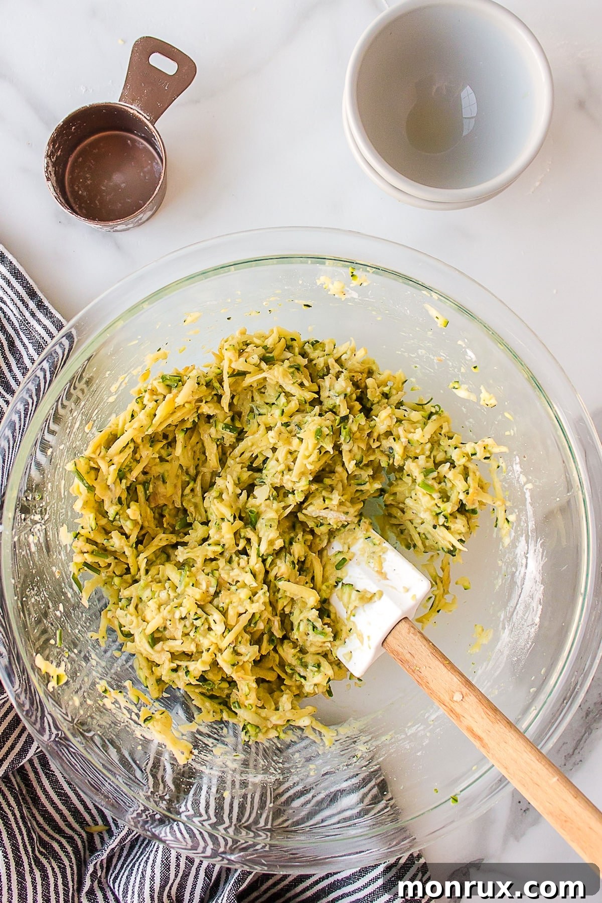A spatula mixing the zucchini and potato fritter batter in a bowl.