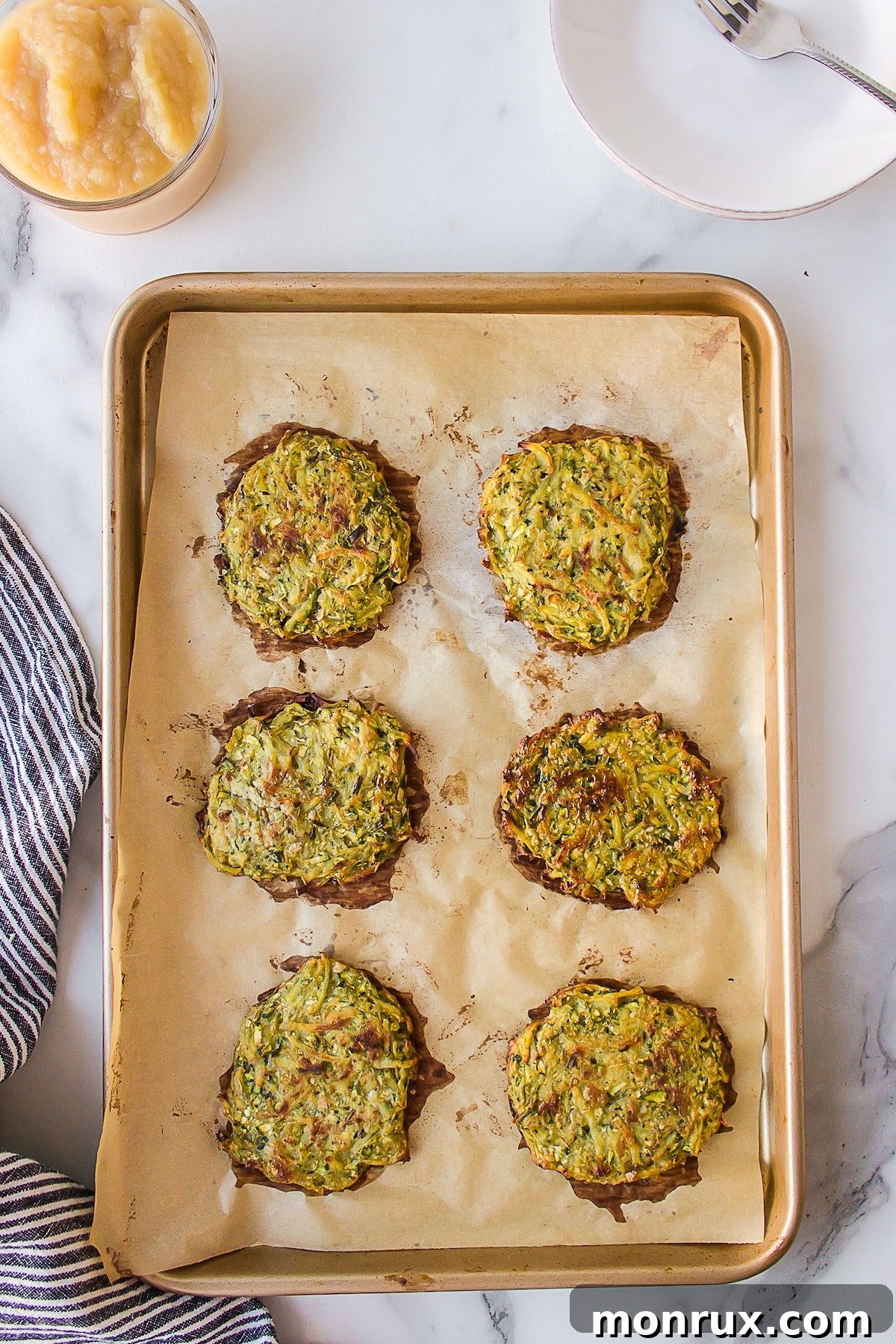 Golden-brown zucchini potato fritters baking in the oven on a baking sheet, showing their delicious crisp exterior.
