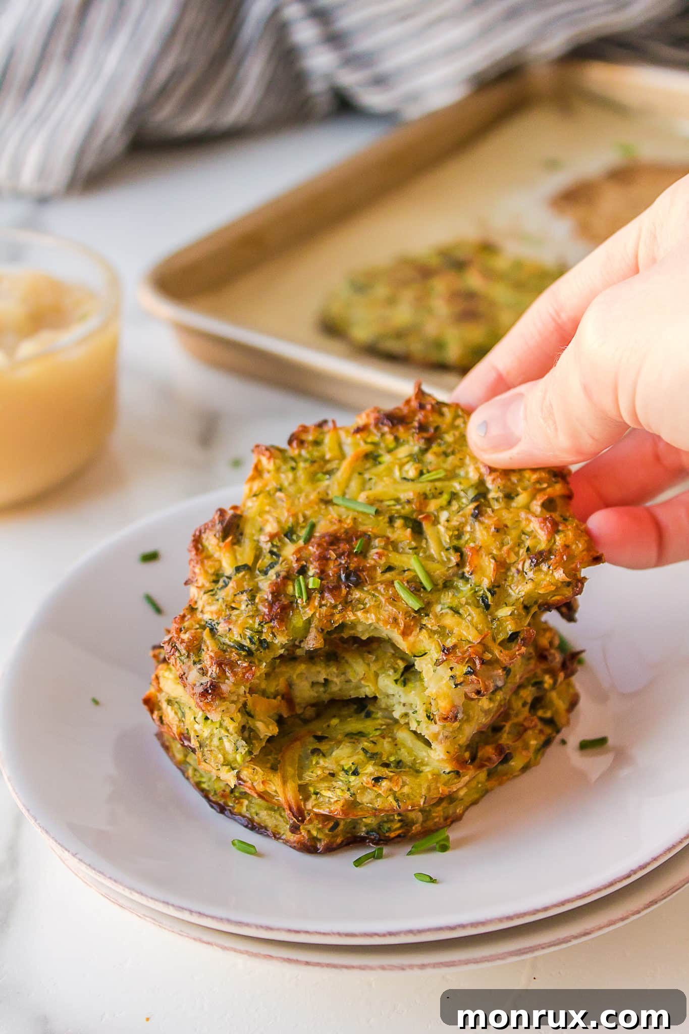 A hand holding a freshly baked, golden-brown zucchini potato fritter, highlighting its crispy texture.