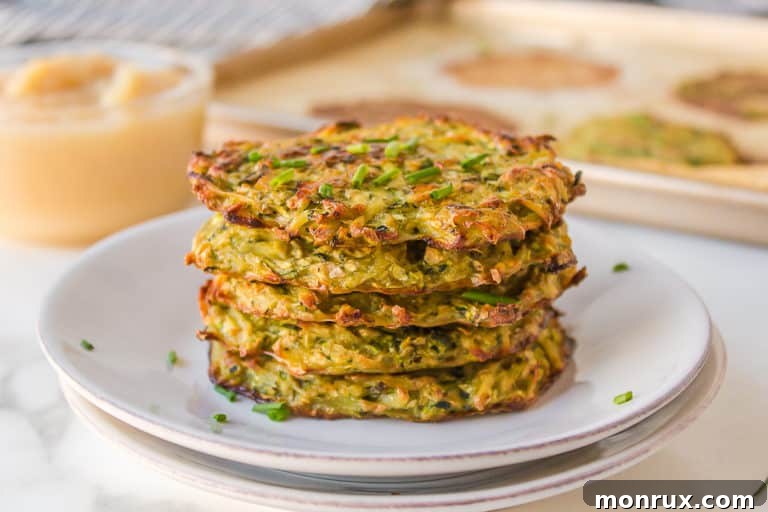 A stack of crispy, golden-brown baked zucchini potato fritters on a clean white plate.