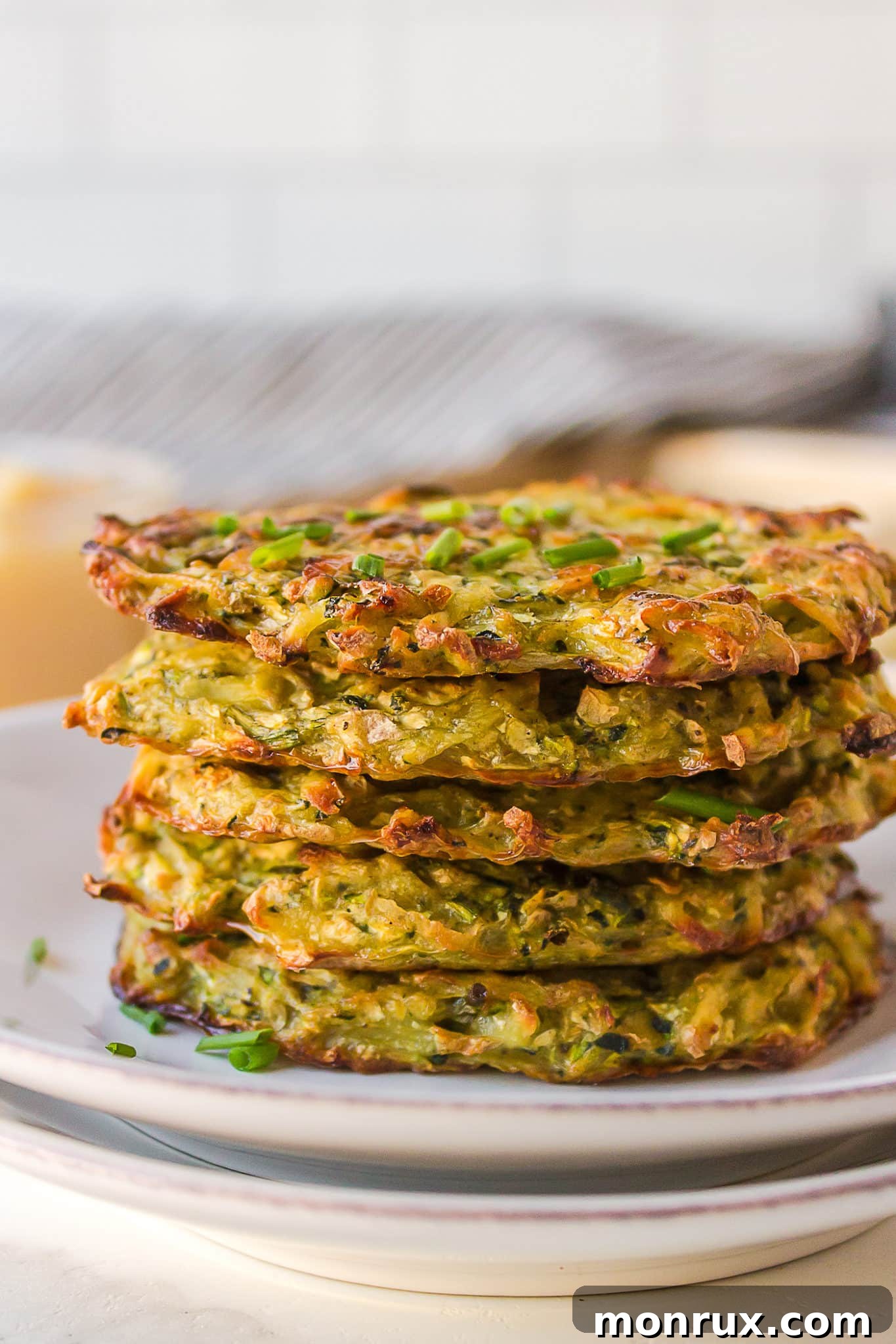 A beautifully arranged stack of baked zucchini potato fritters, garnished with fresh herbs, on a rustic plate.