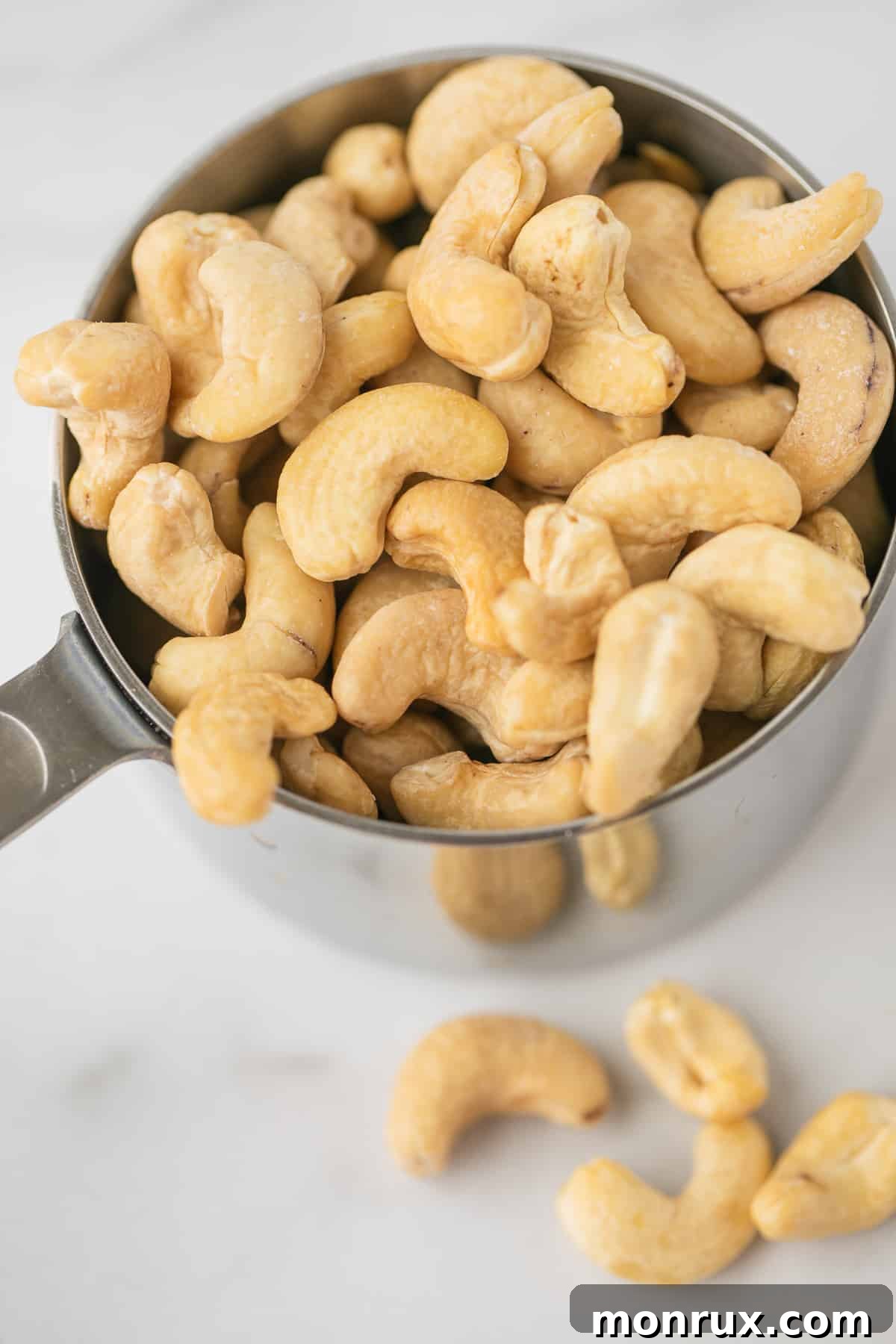 One cup of raw cashews neatly measured in a clear glass measuring cup.